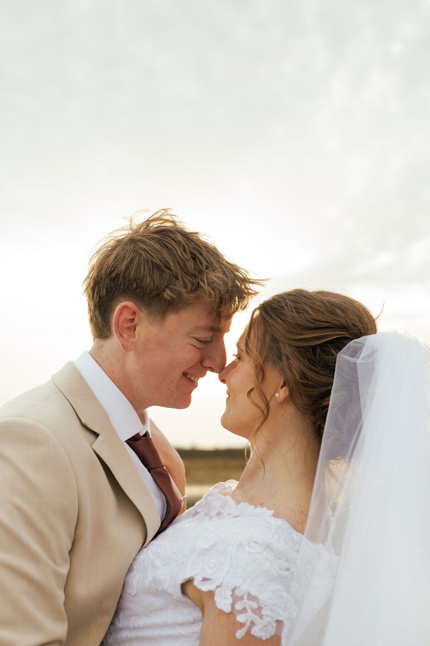 Romantic wedding couple in cream suit and white dress sharing an intimate moment.