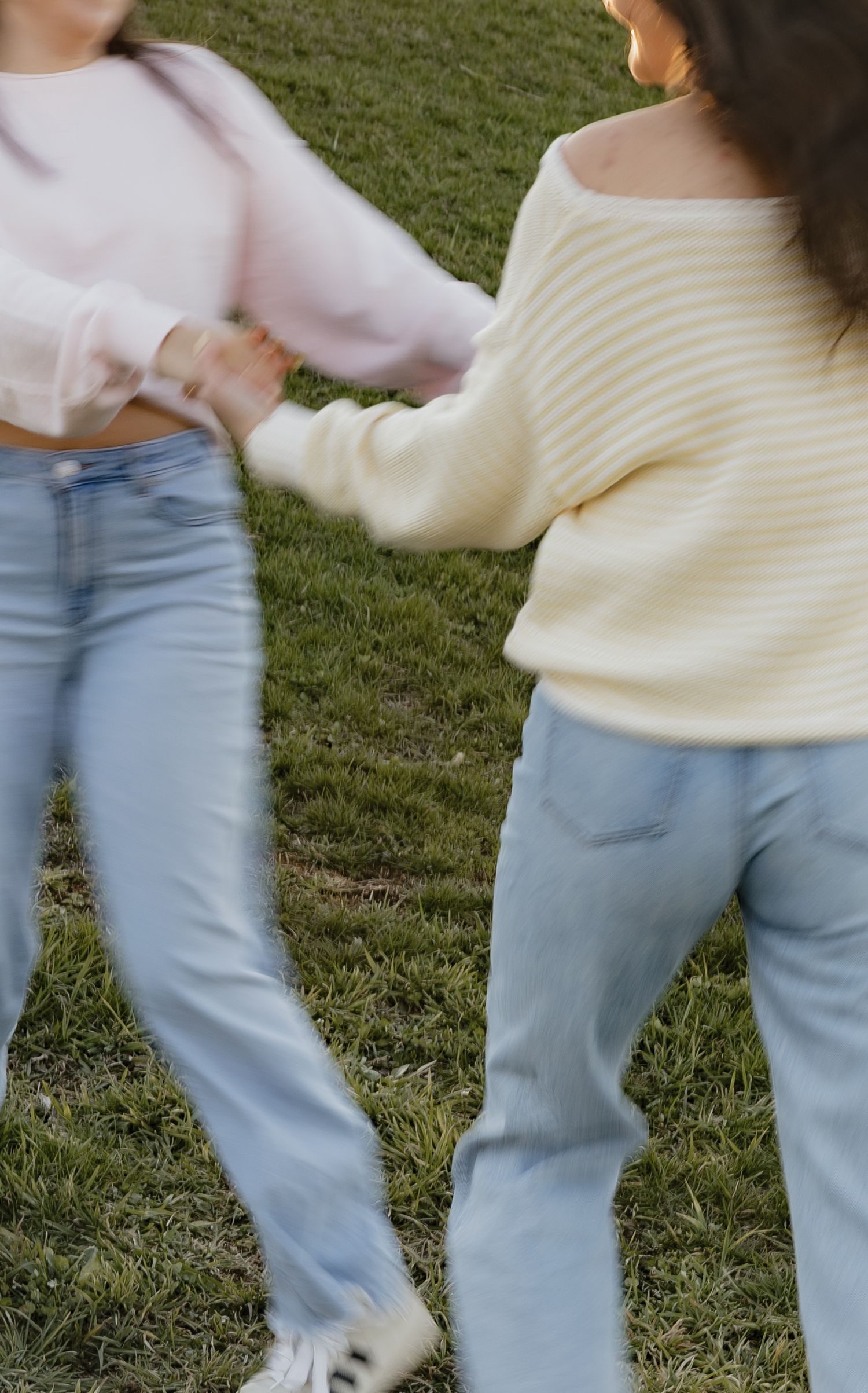 Motion blur captures someone walking on grass wearing light blue jeans and a cream sweater.