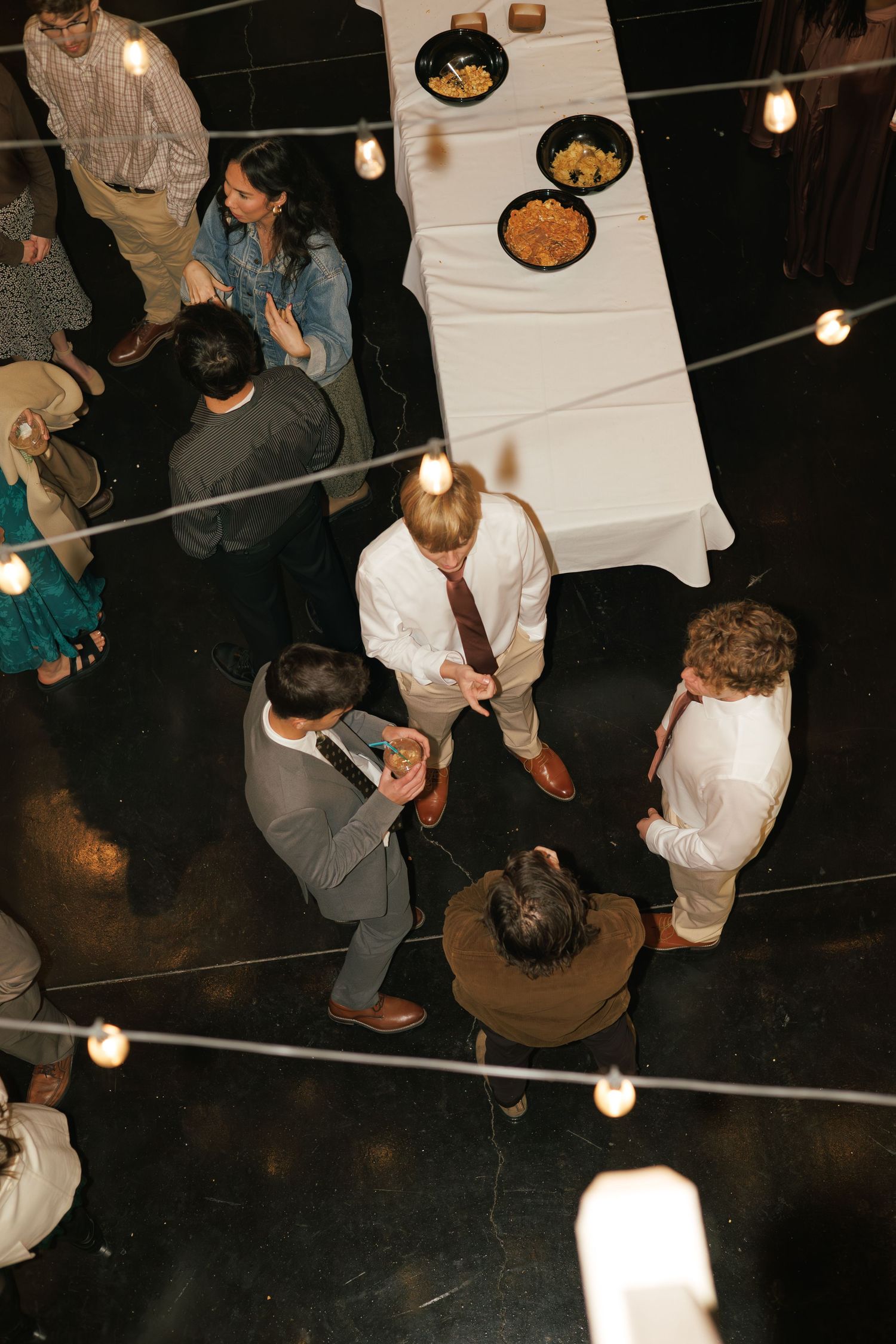 Overhead view of wedding guests dancing on a dark dance floor with string lights above.