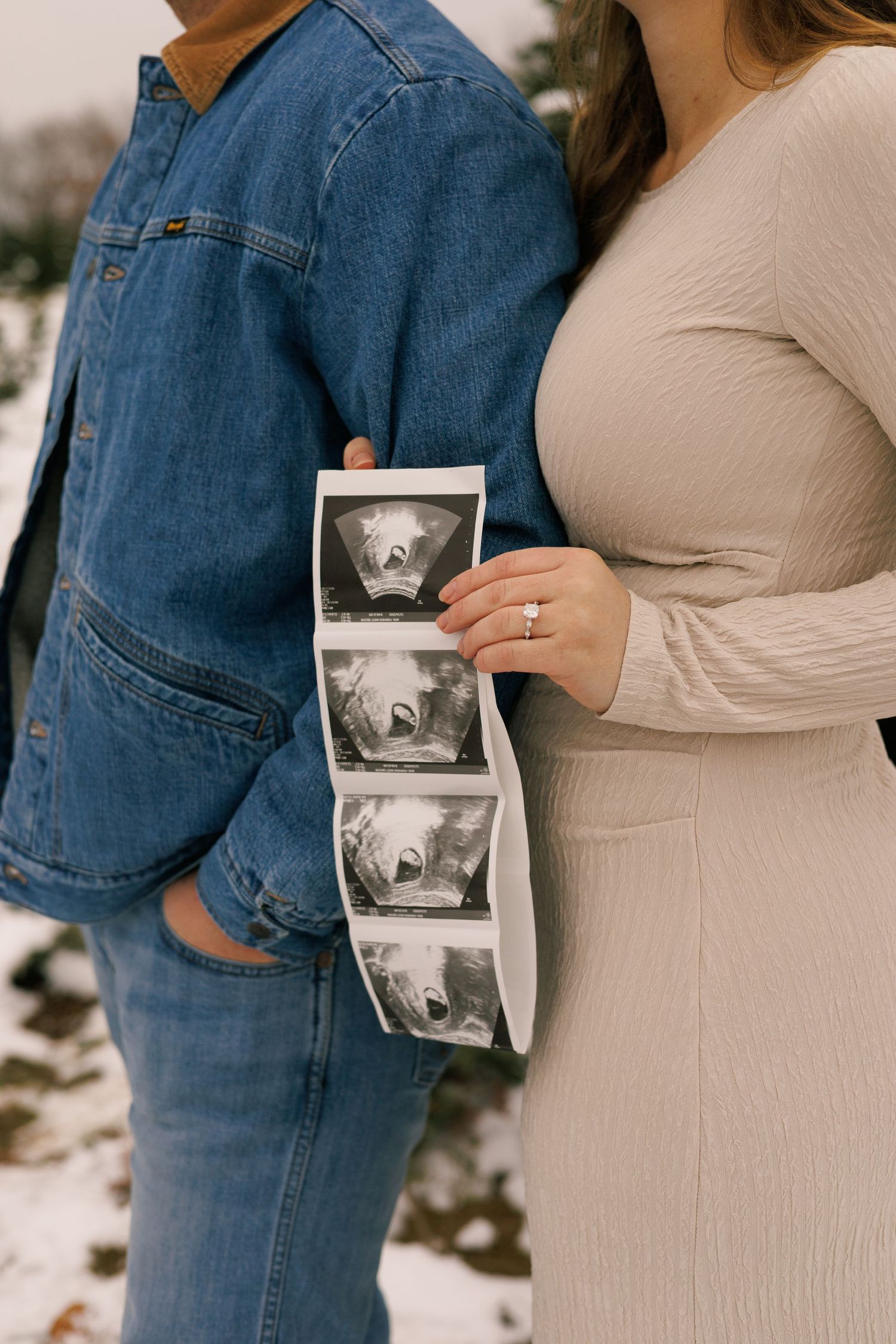 A couple in casual attire holds a sonogram photo during a winter pregnancy announcement.