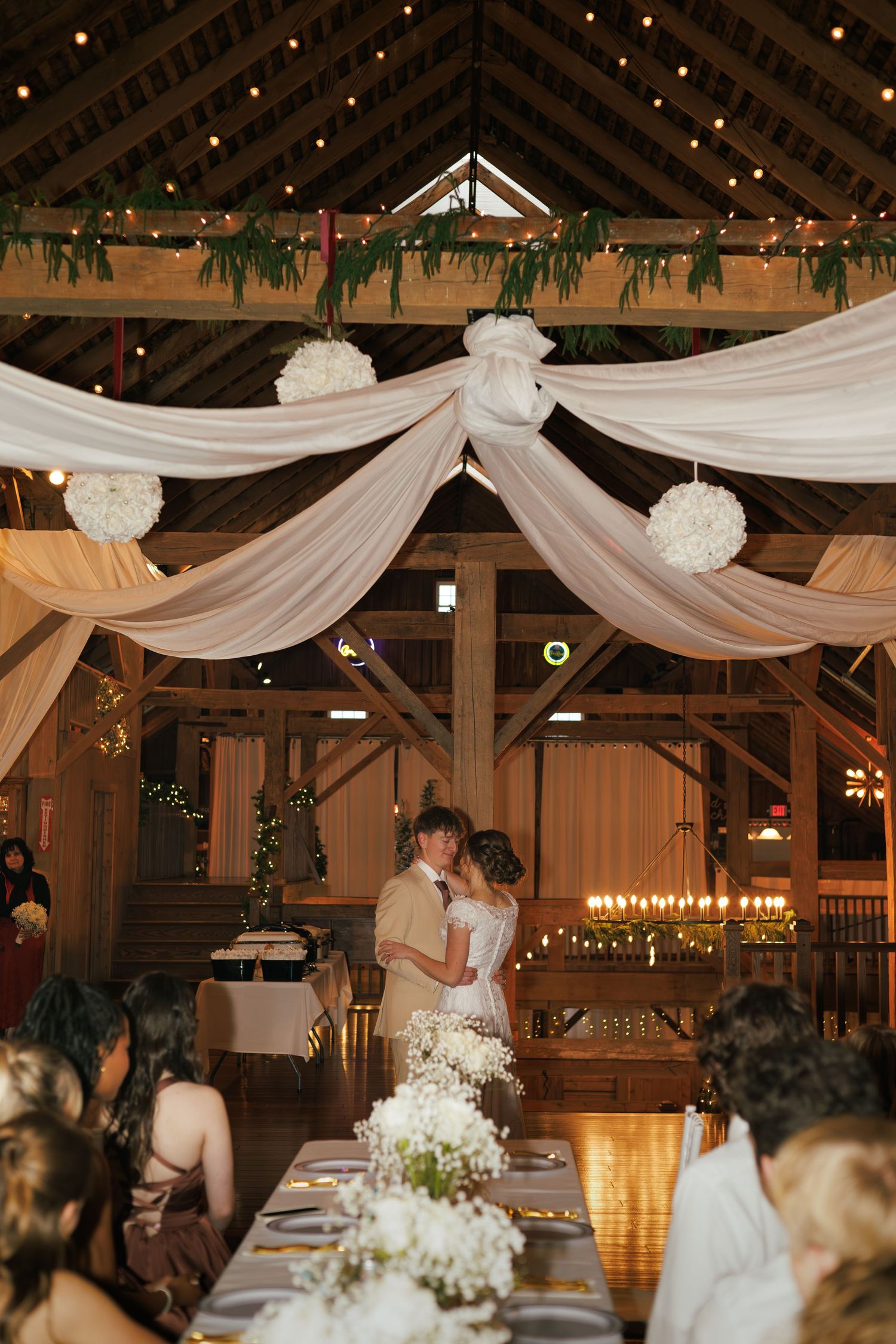 Elegant barn wedding reception with white draping, string lights and floral decorations.