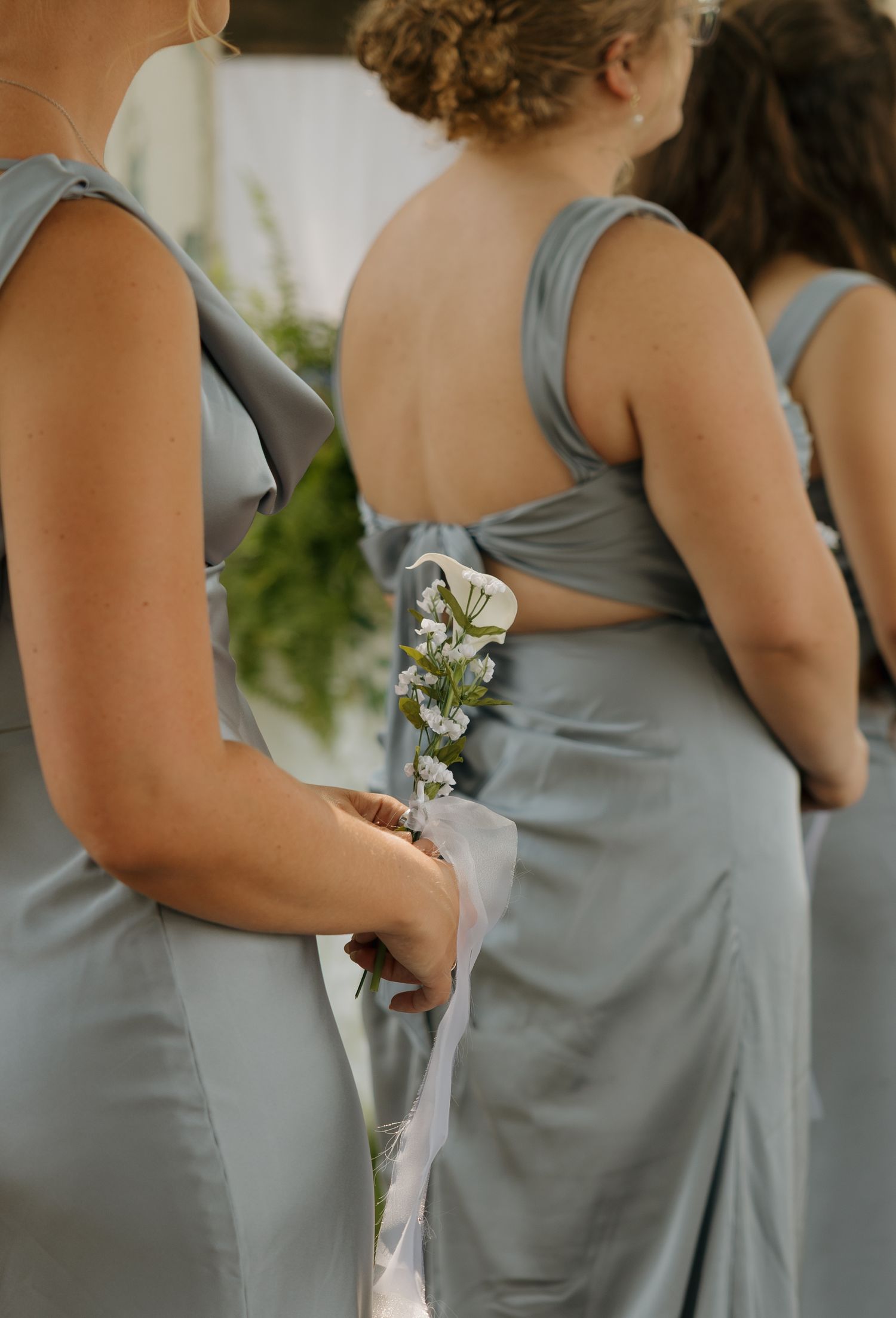 Bridesmaids in elegant dusty blue satin dresses holding delicate white floral bouquets.