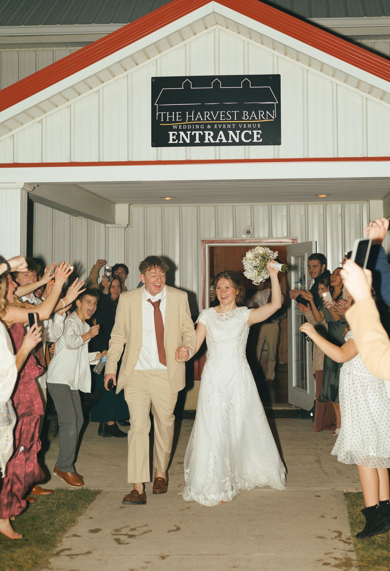 Wedding guests dancing in front of The Harvest Barns entrance sign.