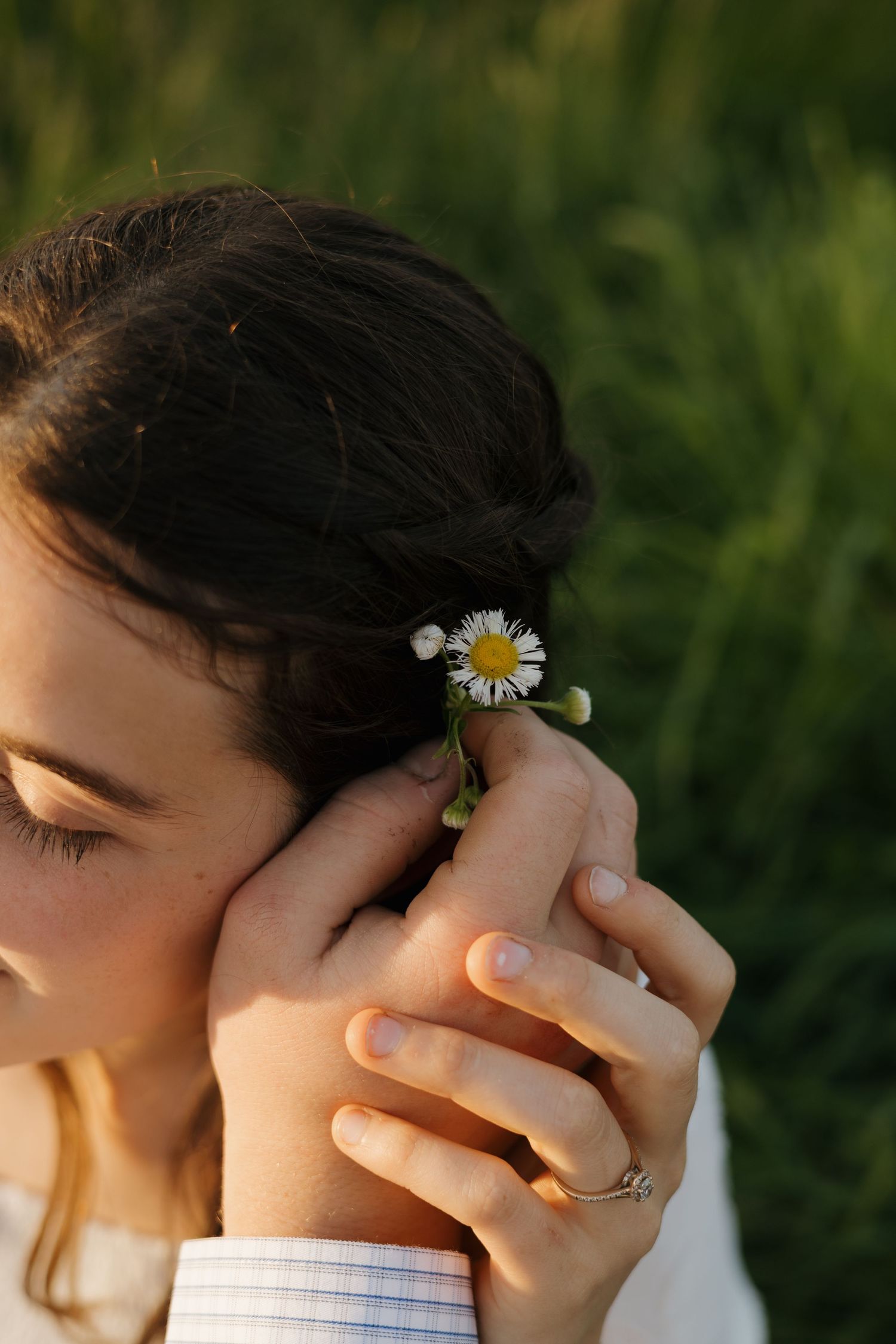 Close-up of hands placing a small daisy flower in a woman's dark hair outdoors.