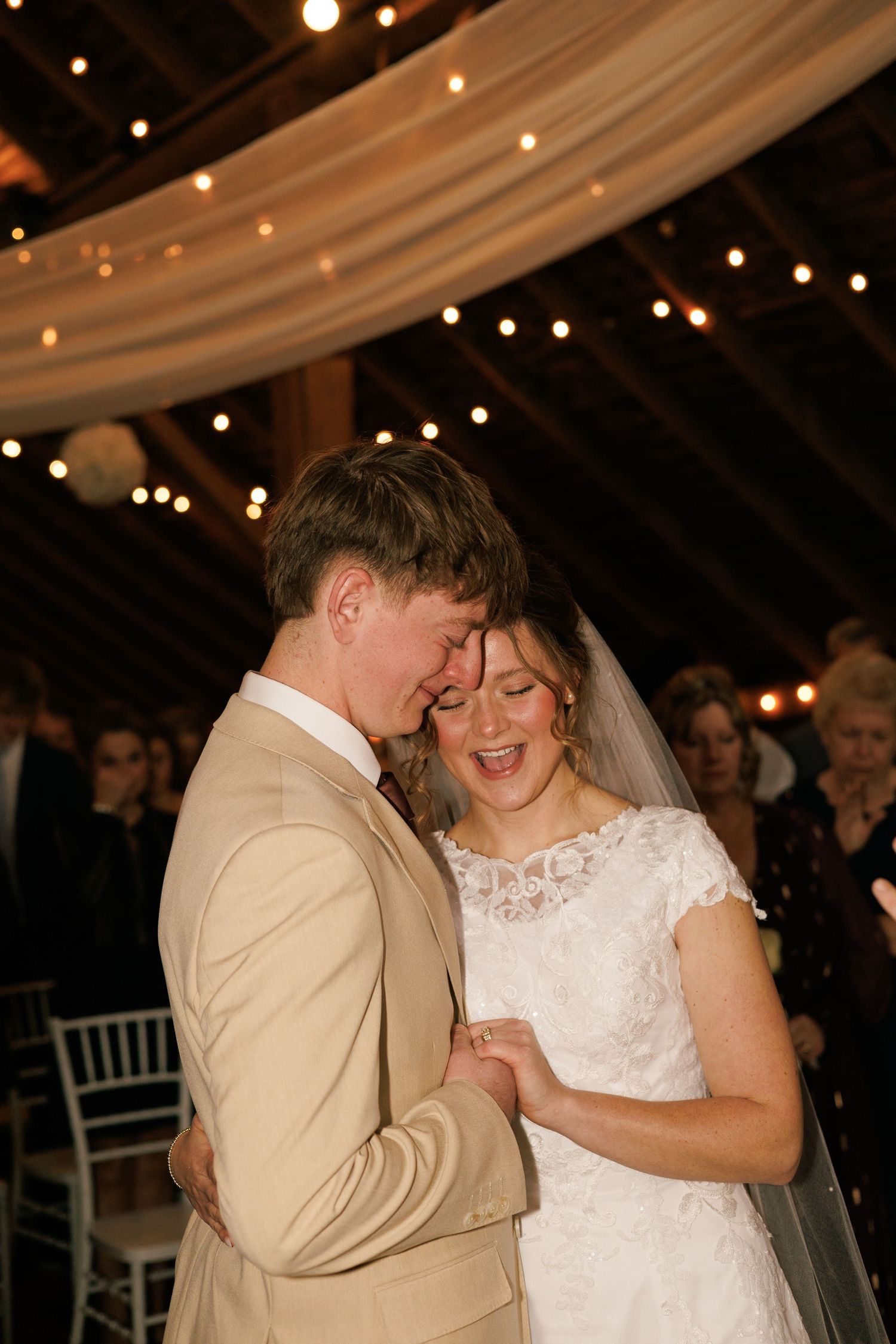 A romantic first dance between newlyweds under twinkling lights at a rustic barn reception.