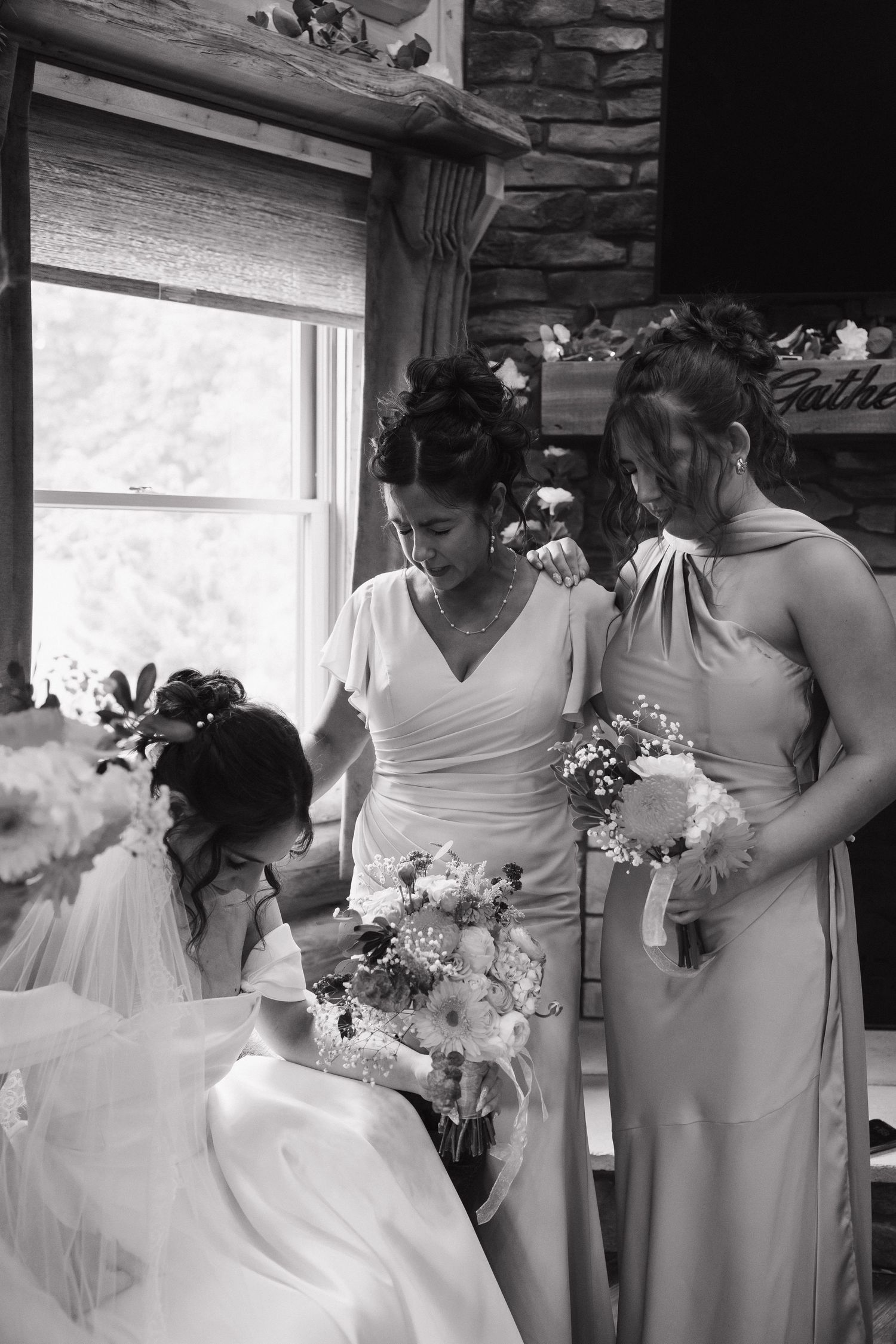 Black and white photo of bride and bridesmaids holding floral bouquets inside a rustic wedding venue.