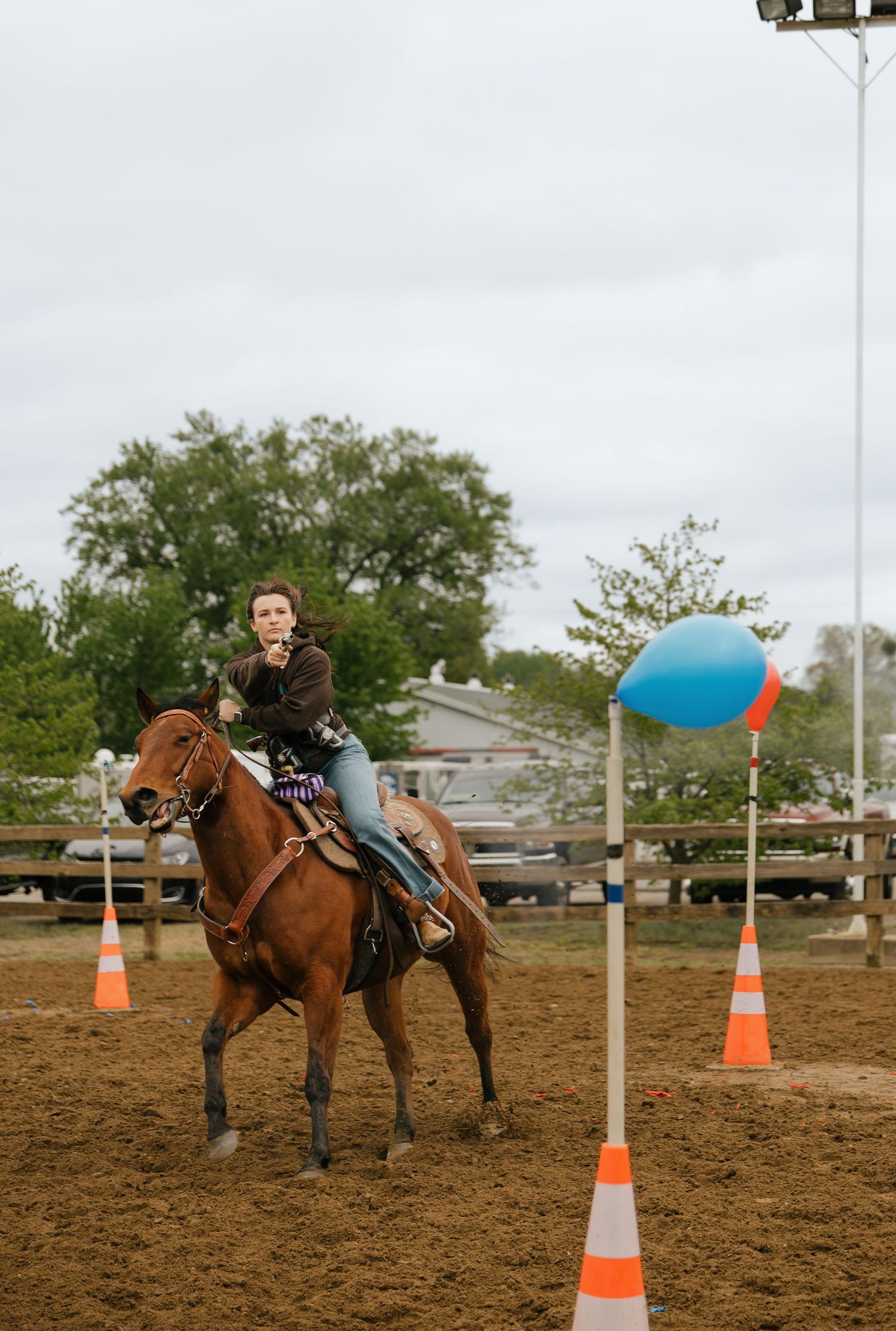 Young rider on chestnut horse navigating orange cone course with colorful balloon markers at outdoor equestrian event.