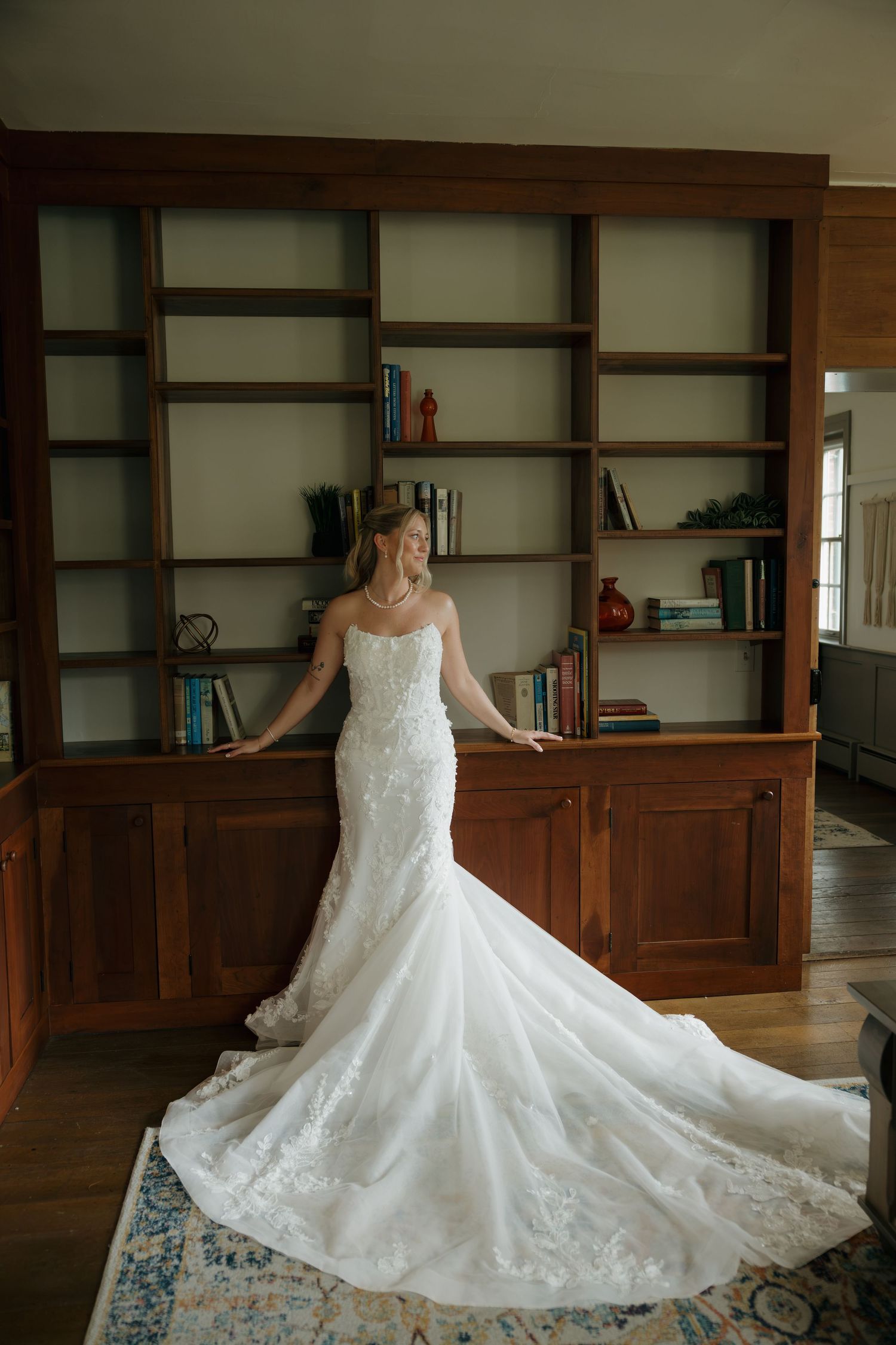 Bride in a stunning white lace mermaid wedding gown with a long train posing in an elegant wood-paneled library.