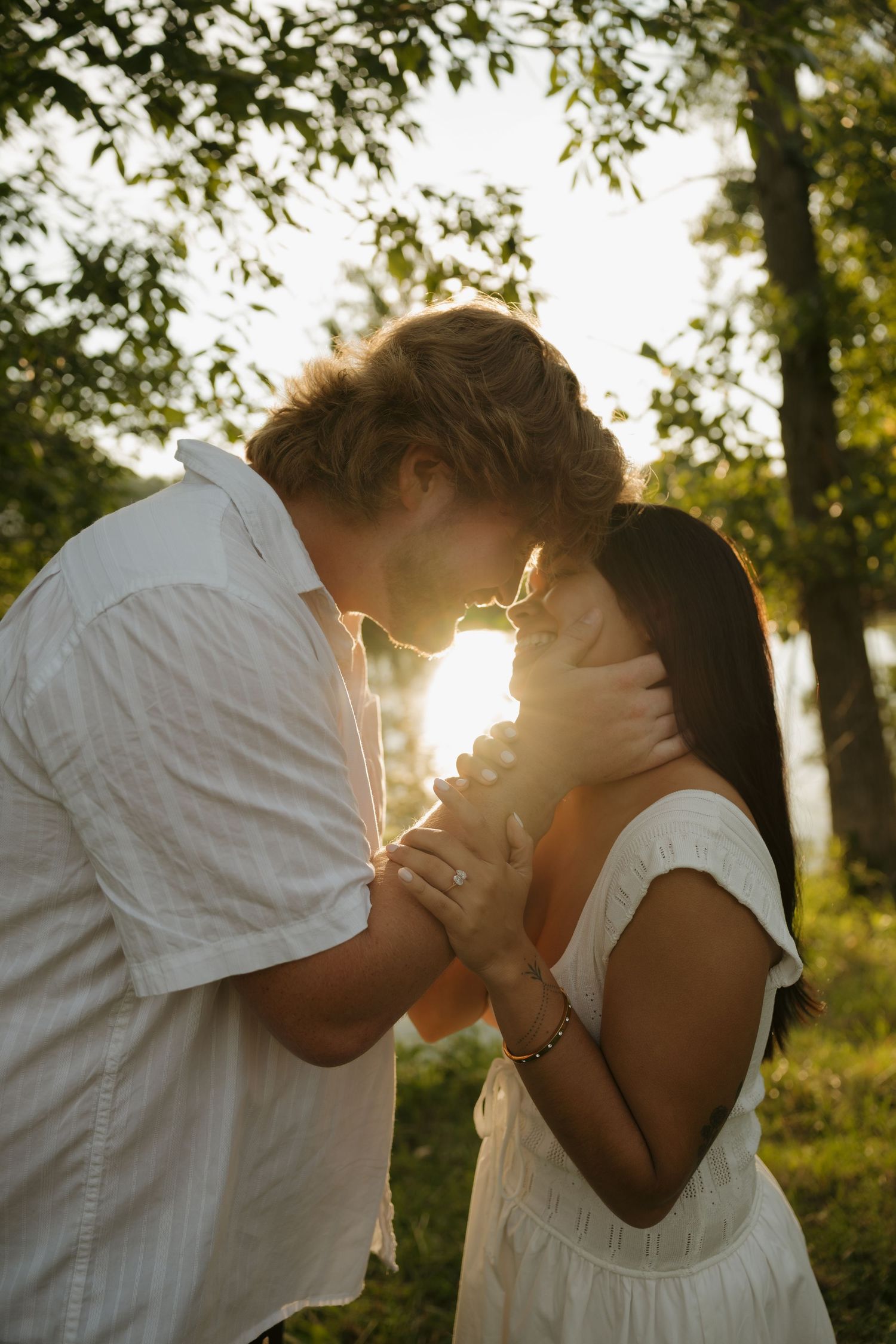 Couple sharing a romantic moment at golden hour in a sunlit park, wearing white outfits.