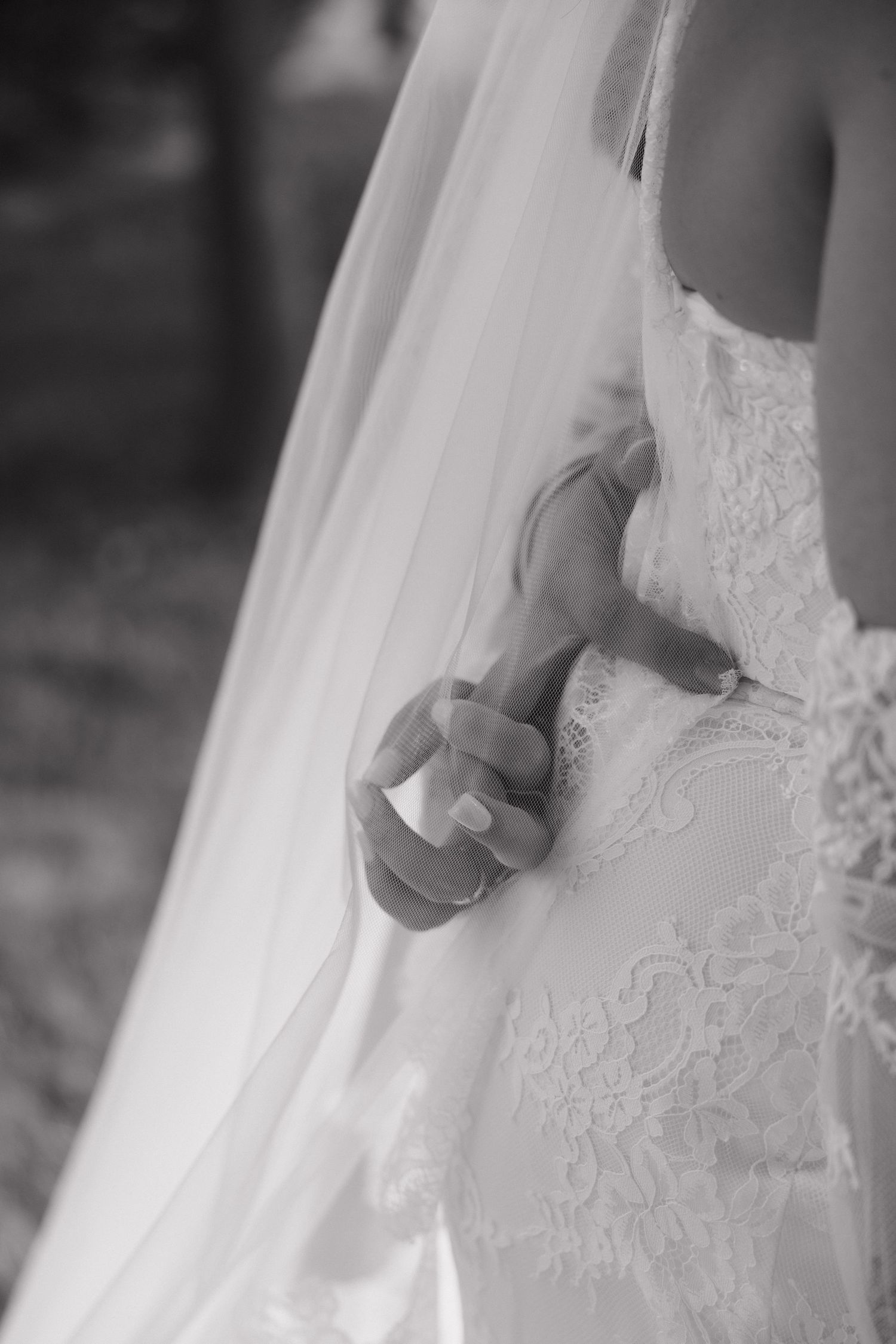 Black and white close-up of a bride holding her lace wedding dress and veil with manicured hands.