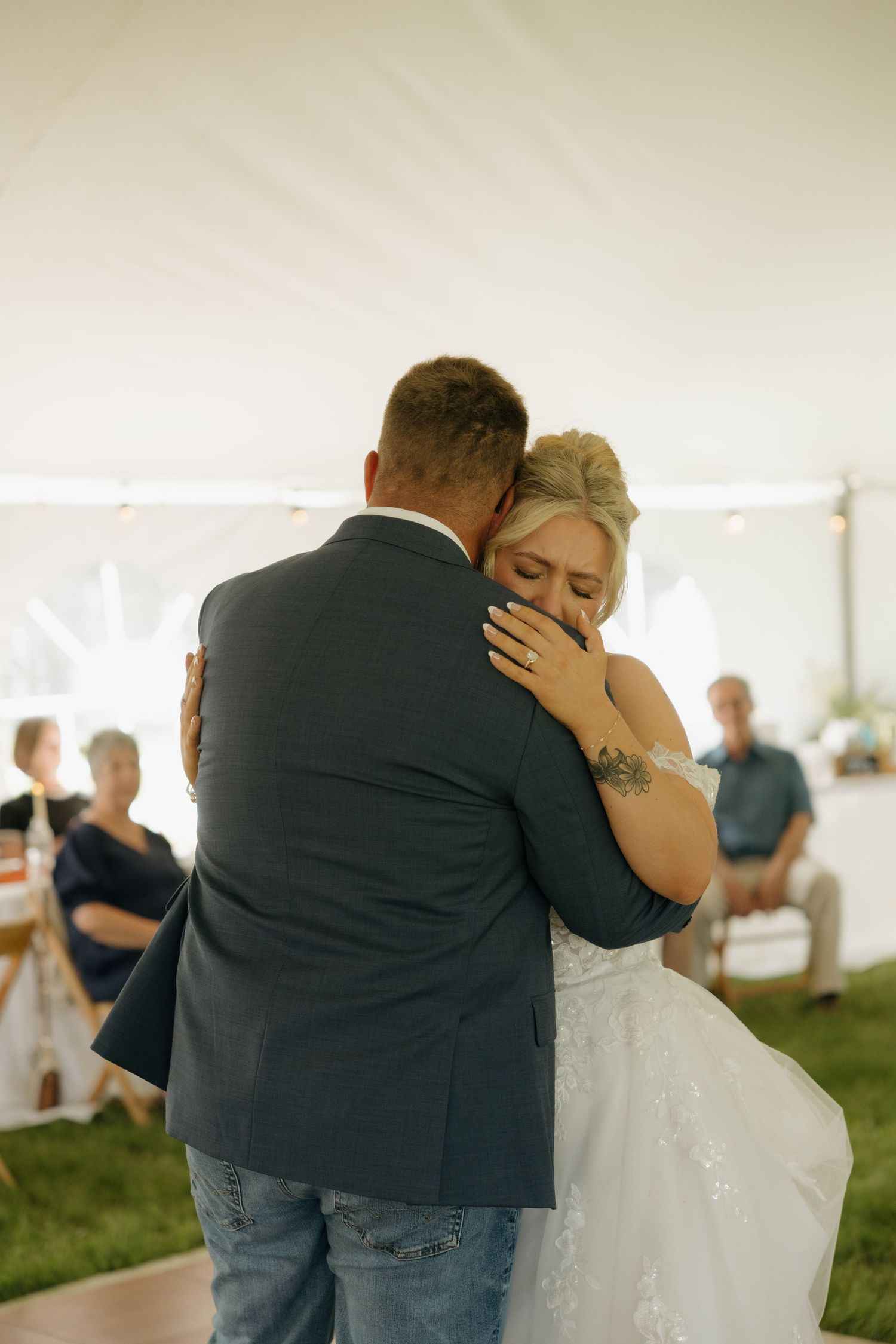 Emotional bride and groom sharing their first dance embrace under a white tent.