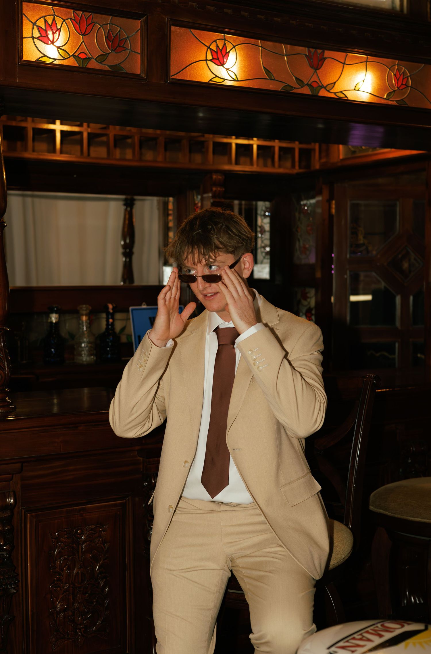 Person in a tan suit covering their face while dancing in a dimly lit room.