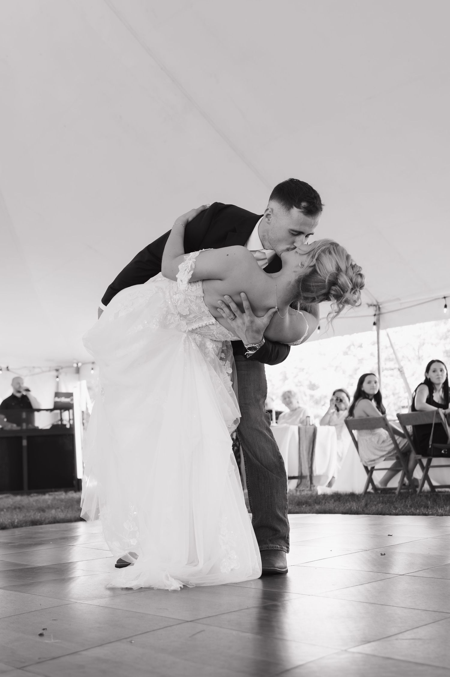 Groom dips bride for a romantic kiss during first dance at outdoor tented wedding reception.