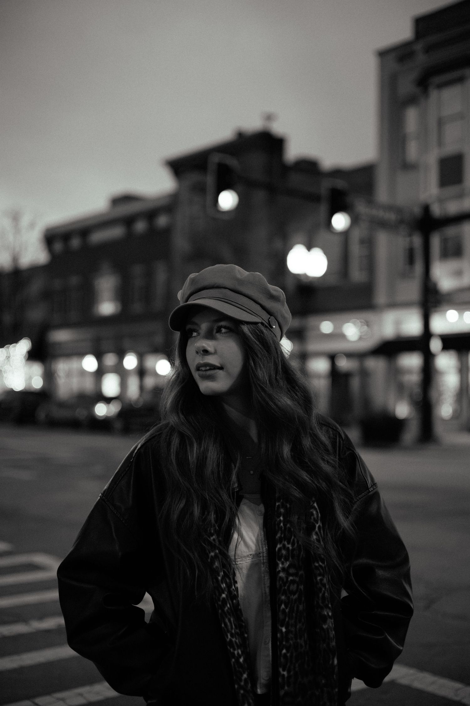 Moody nighttime street photography of a person wearing a newsboy cap and winter coat against city lights.