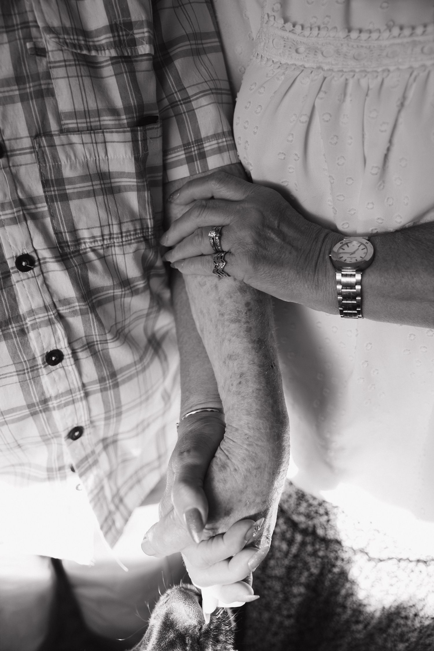 Black and white photo of two people holding hands, one wearing a watch and ring, showing a tender moment of connection.