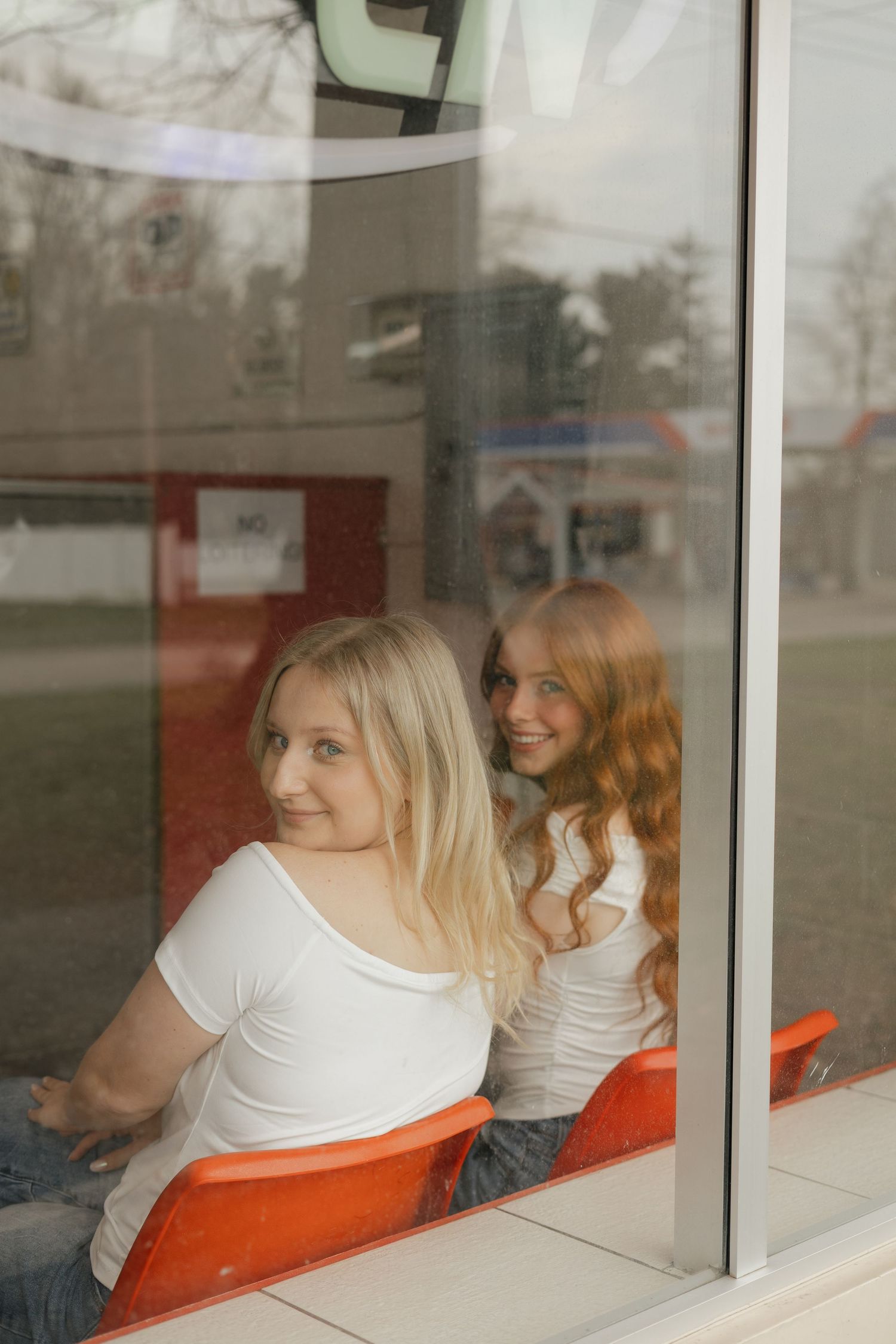 People in white shirts sit at a window counter with orange seats, creating a retro diner-like reflection scene.