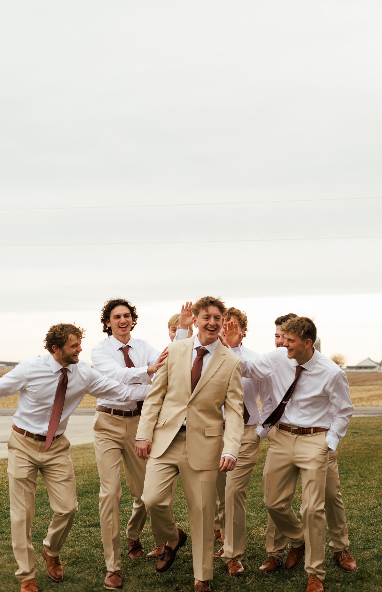 Groomsmen in khaki suits and ties posing playfully outdoors.