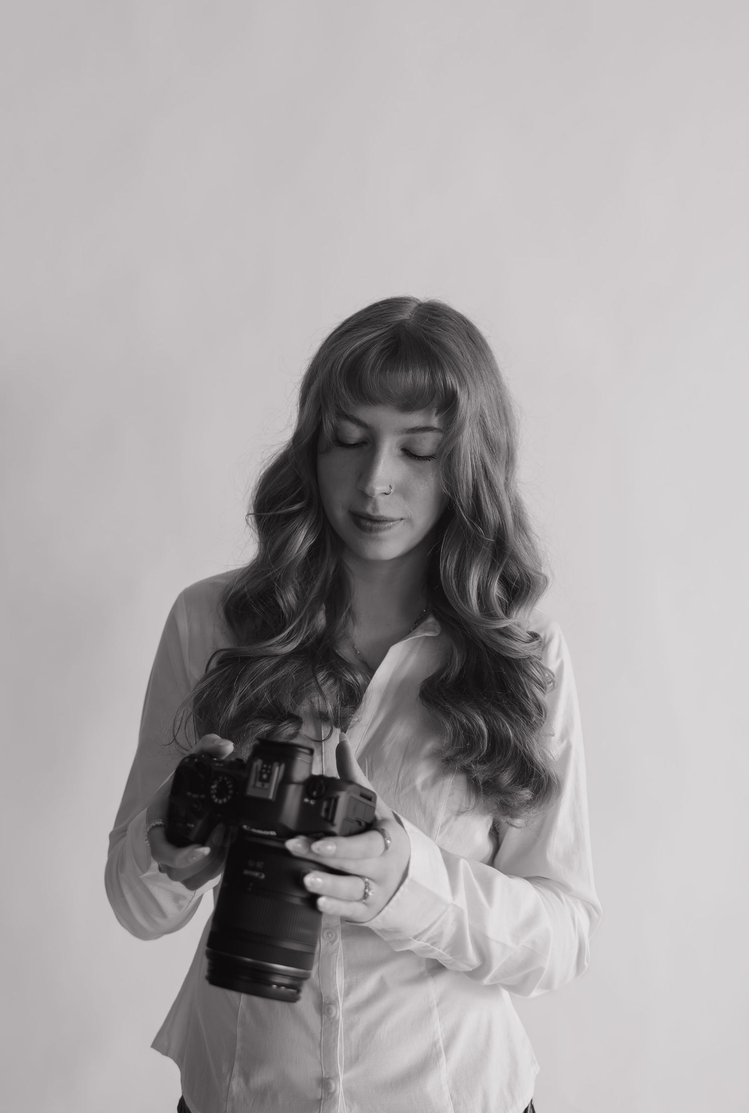 Black and white portrait of a young woman with long wavy hair holding a DSLR camera.