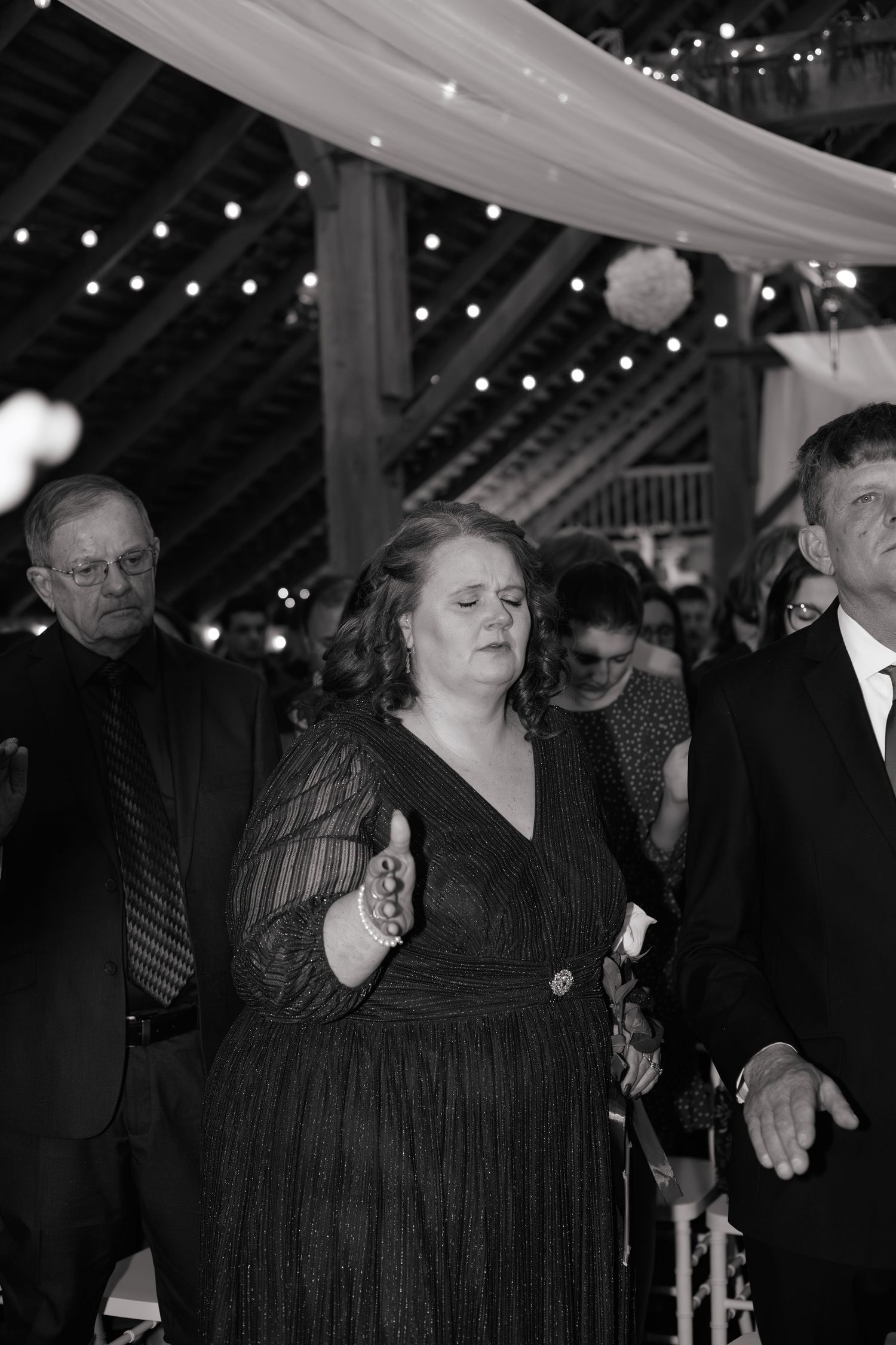 Guests dancing at a wedding reception under twinkling string lights and white fabric draping.
