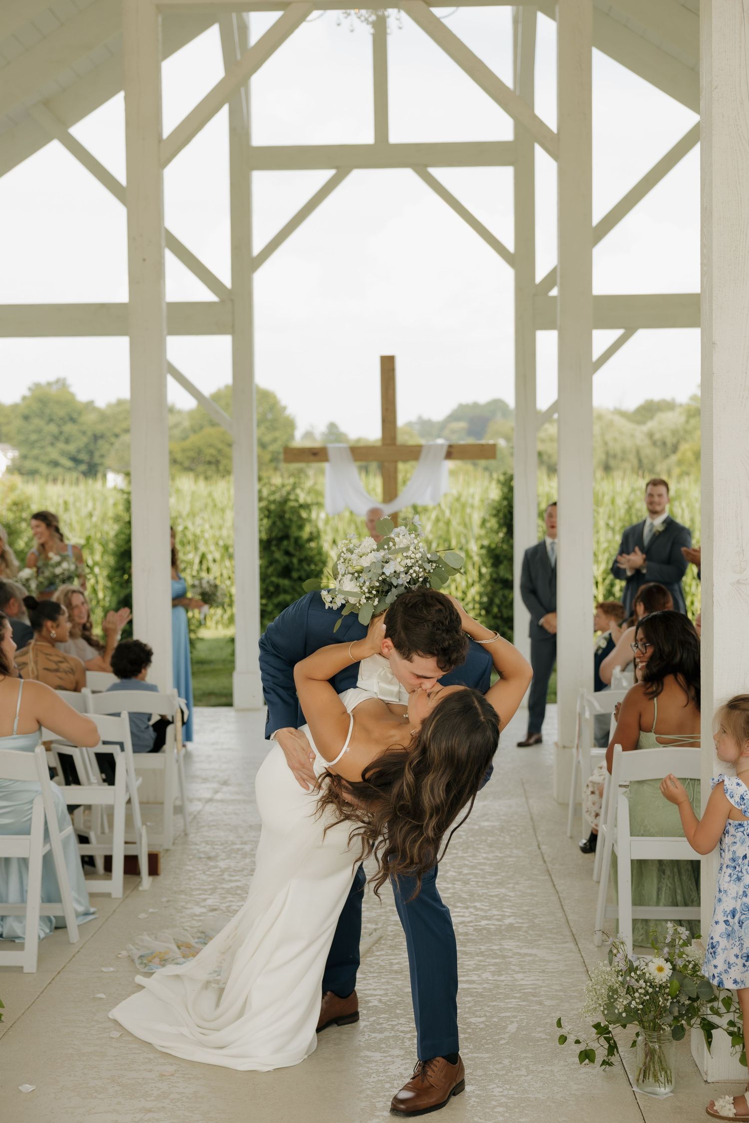 Bride and groom sharing romantic dip kiss at outdoor chapel wedding ceremony aisle.