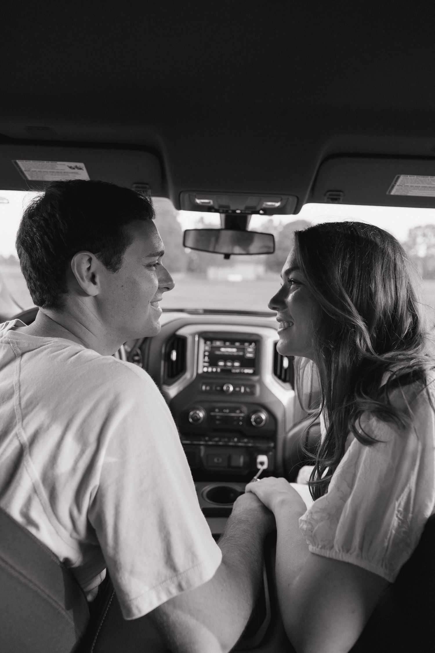 Black and white photo of a young couple sitting in a truck cab, smiling and facing each other romantically.