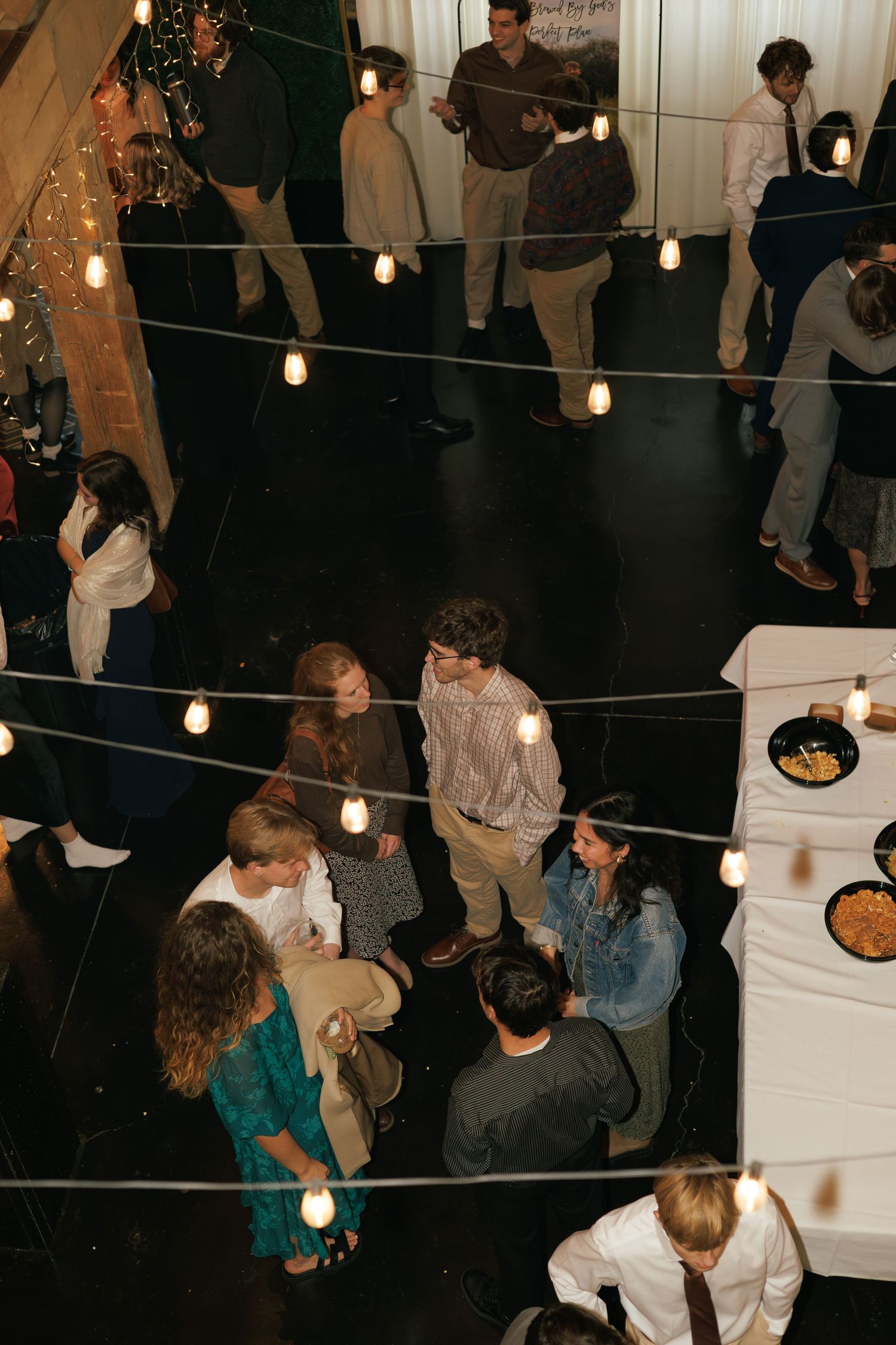 Wedding reception party with string lights and guests mingling in a dark venue.