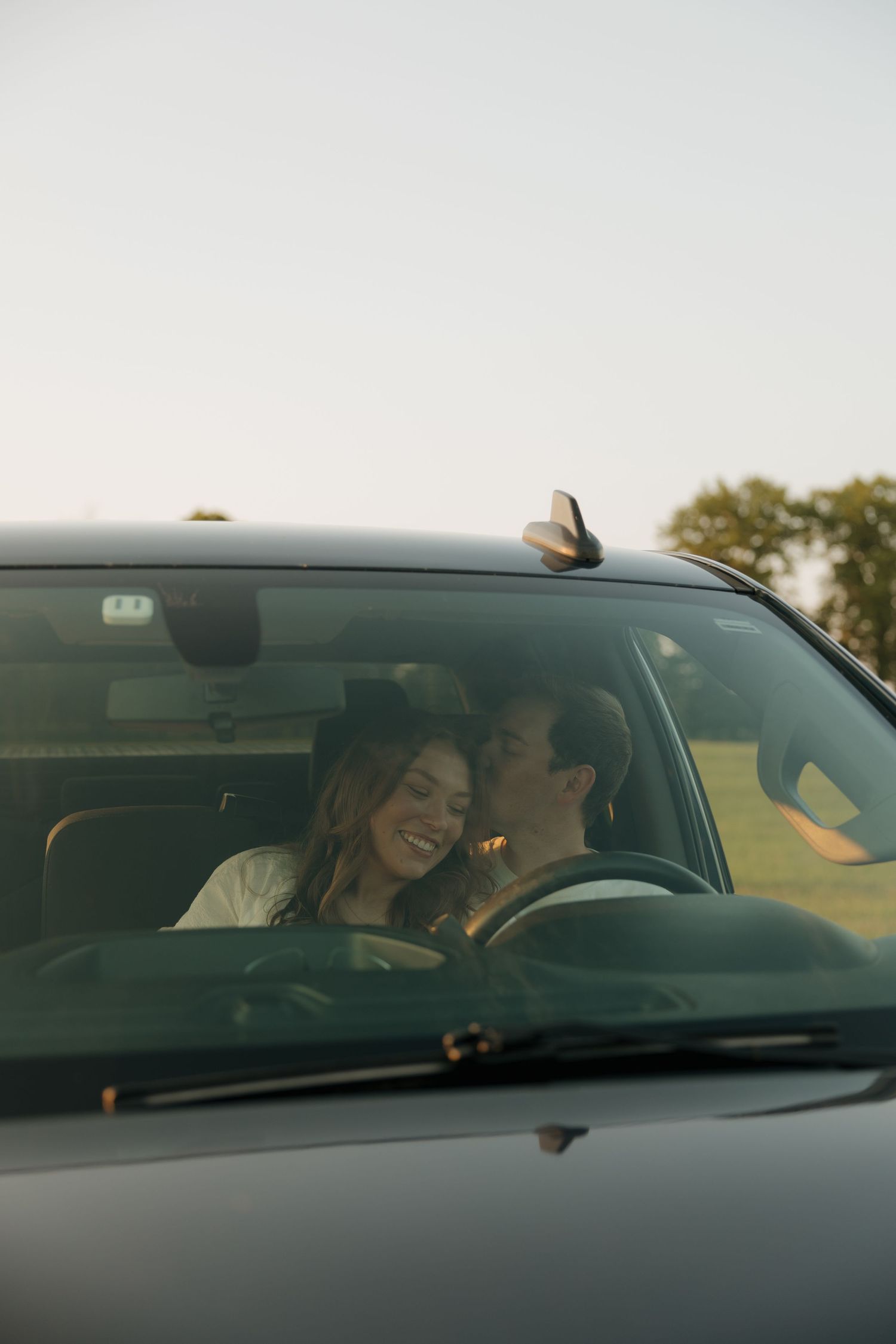 Happy couple sharing an intimate moment inside a car at dusk, woman smiling and leaning toward man.