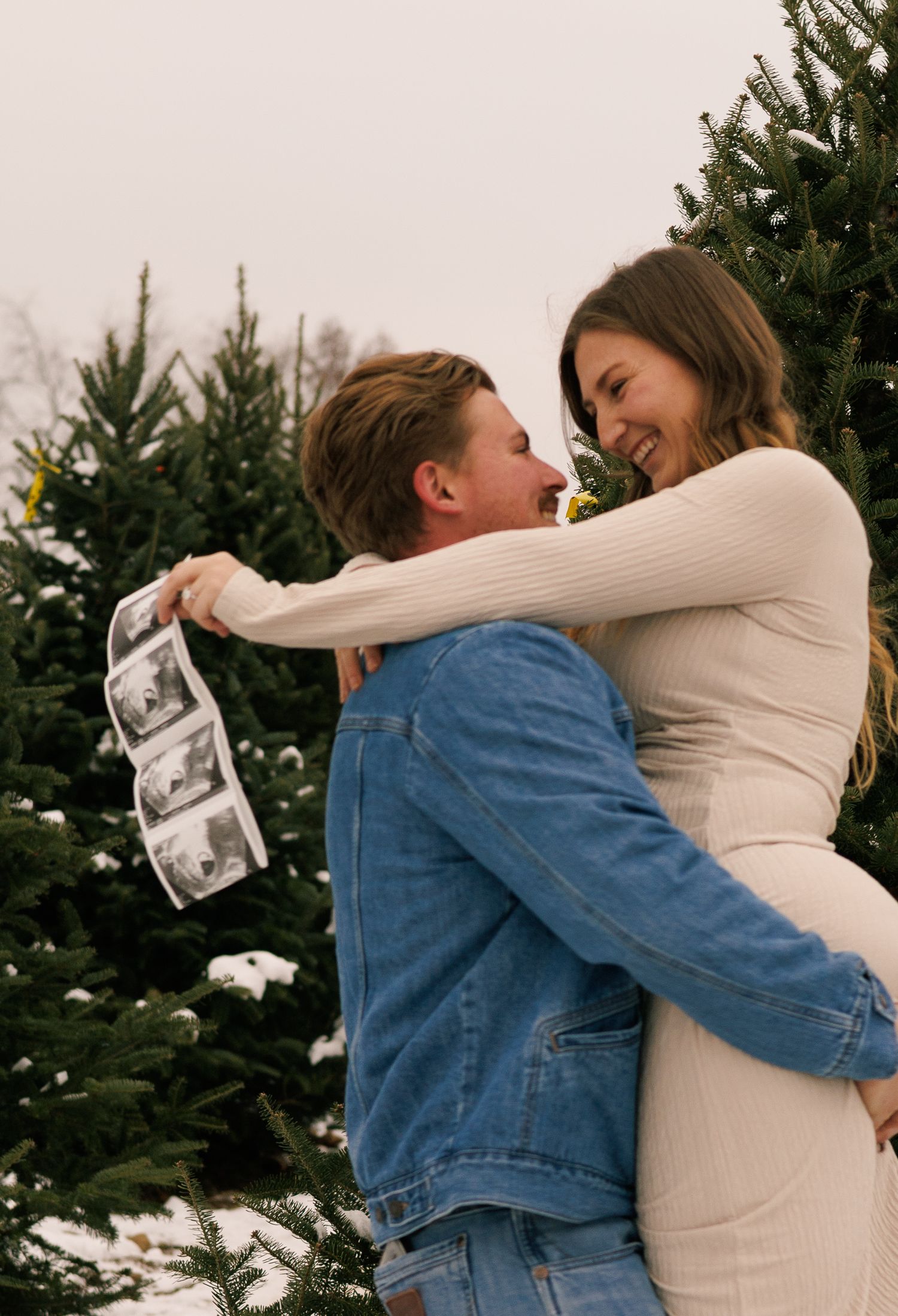 A joyful couple embraces while sharing their pregnancy news in a winter setting.