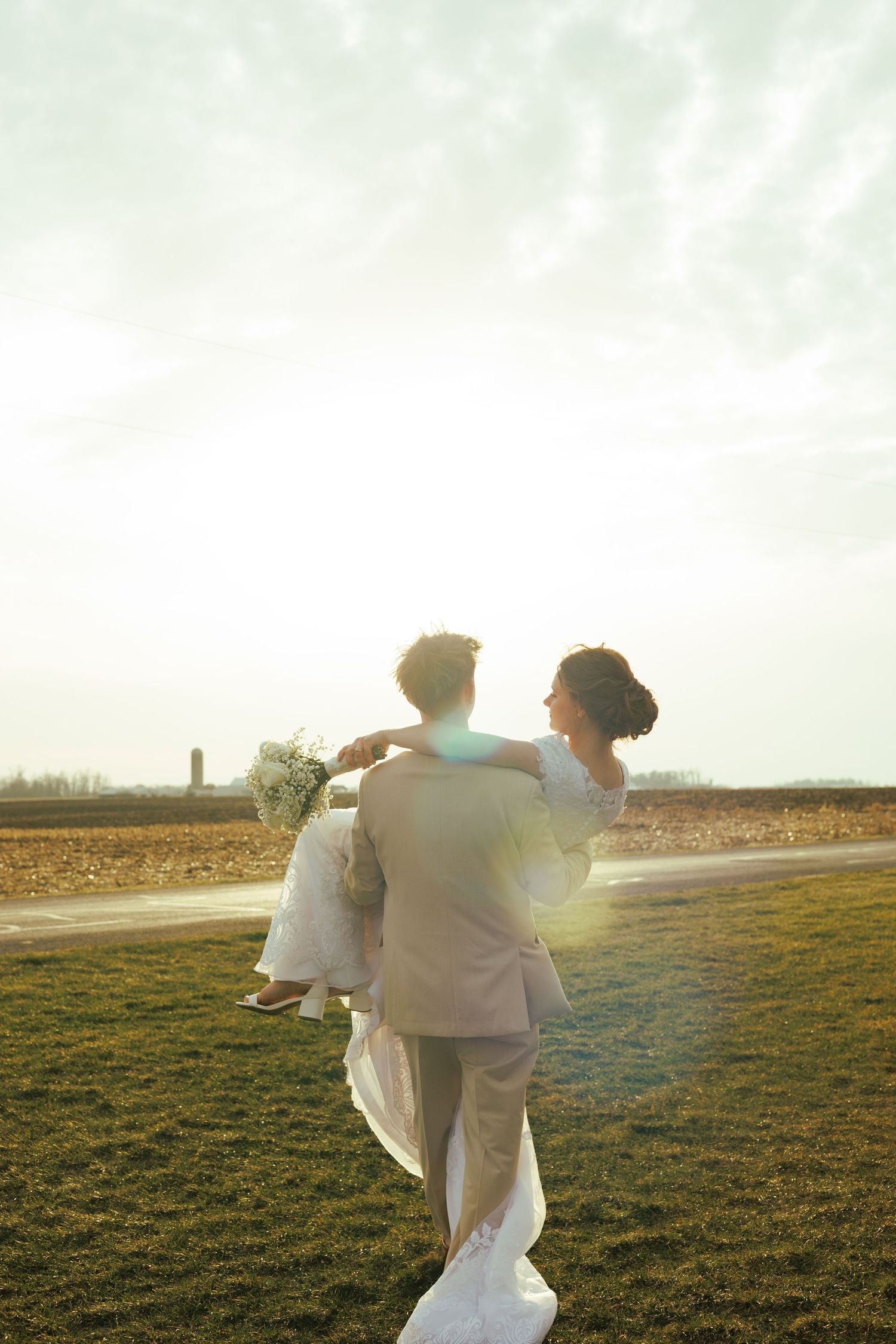 Couple embracing in golden sunset light on a hilltop during their wedding day.