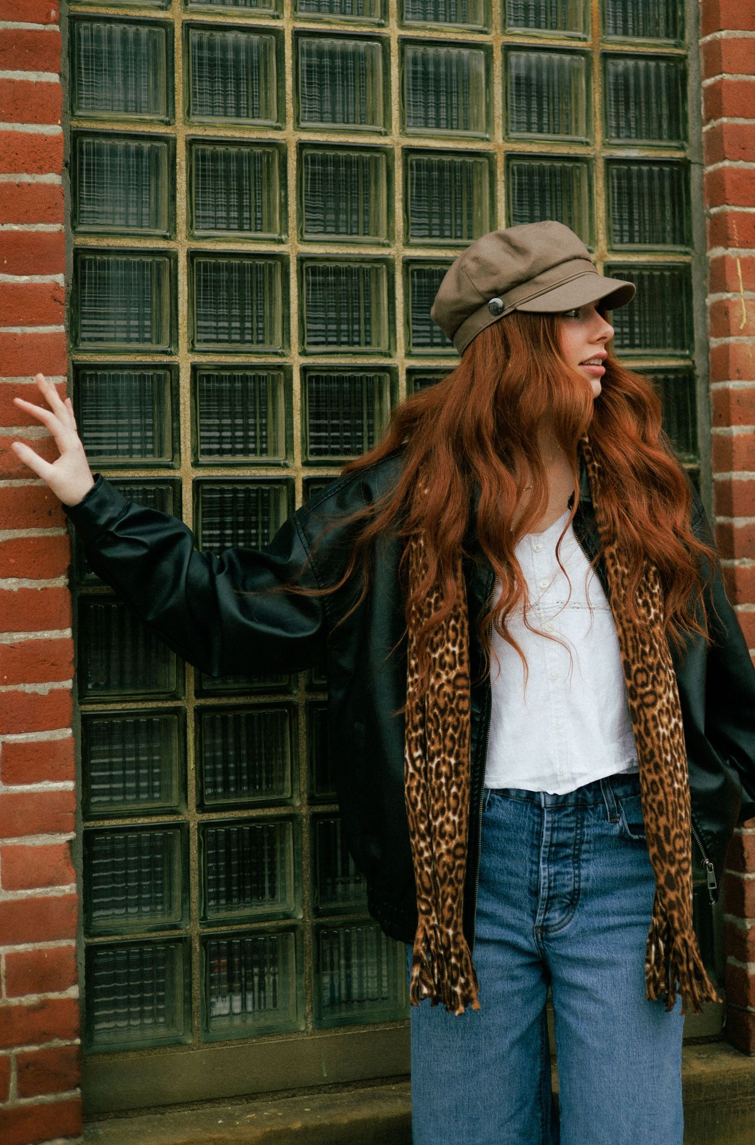 Stylish street fashion with leopard print jacket and newsboy cap against brick wall.