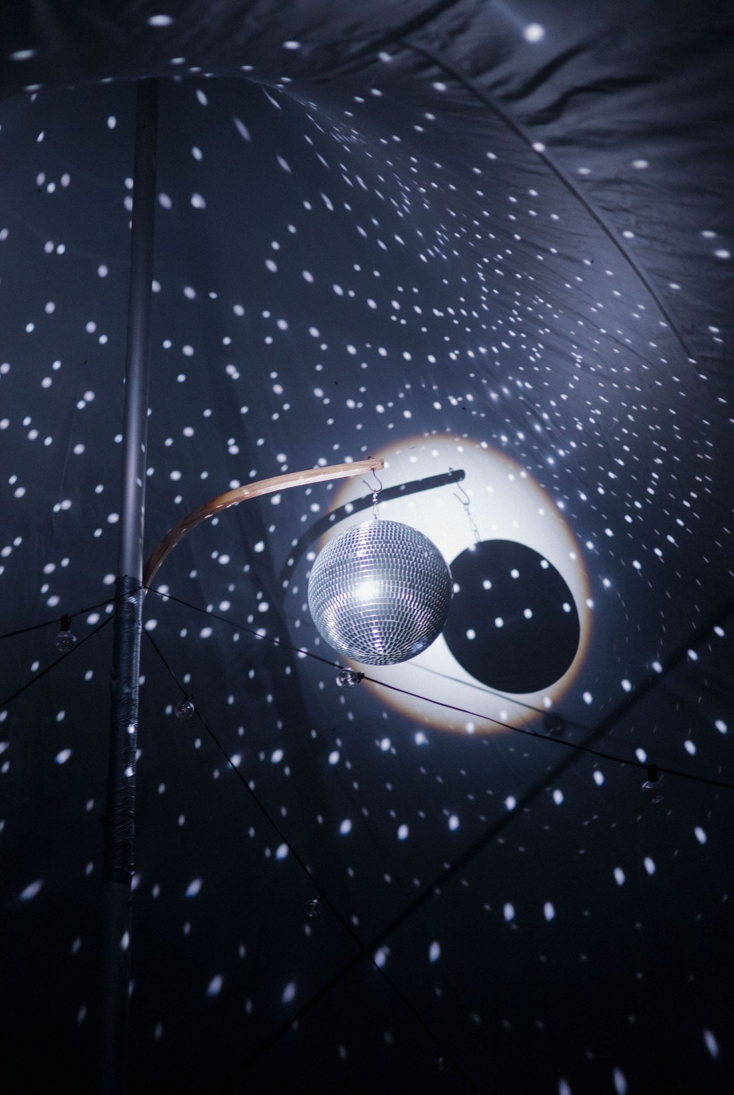 A mirrored disco ball reflecting light dots onto a dark umbrella interior, creating a starry night effect.