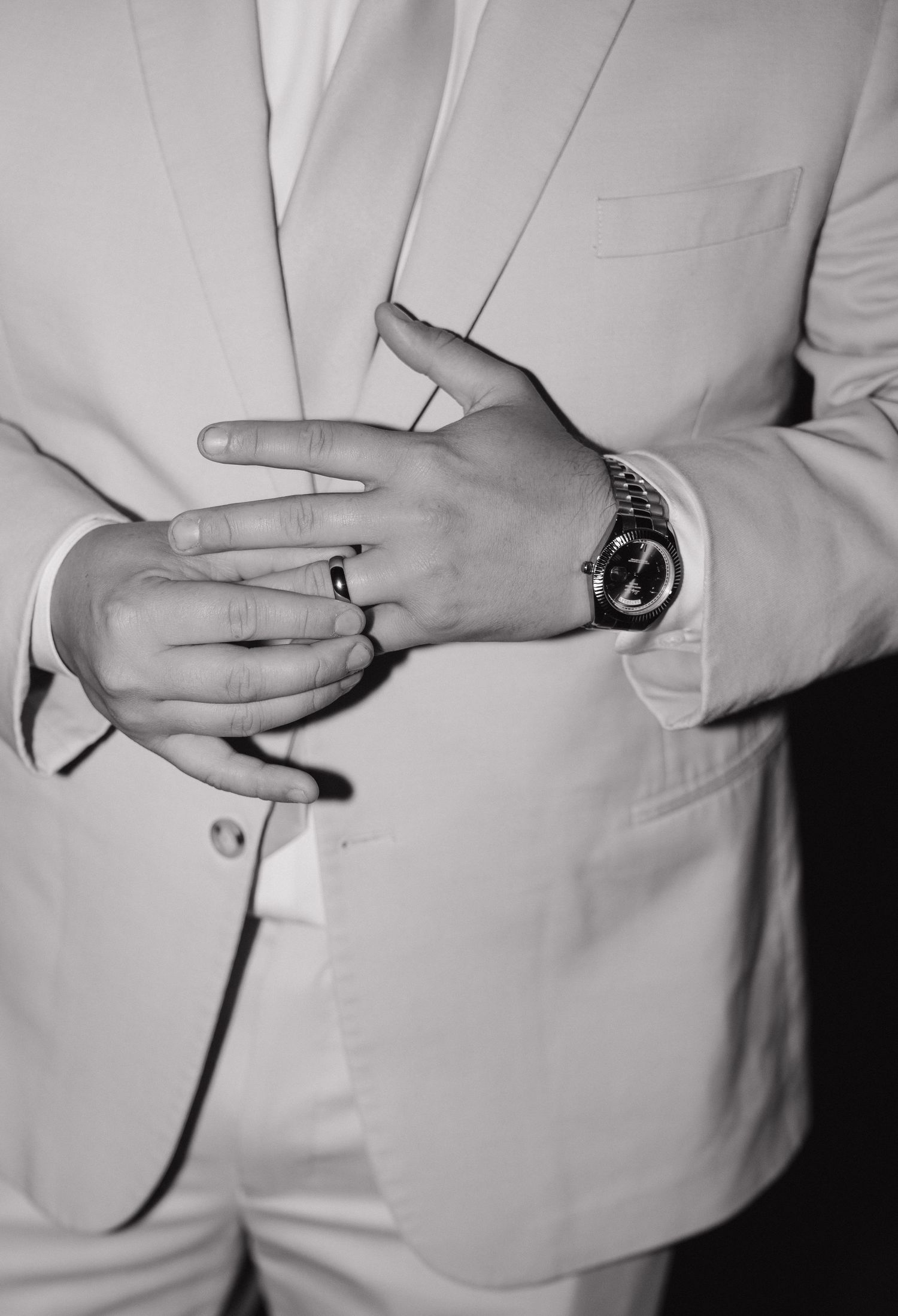 Groom in white suit adjusting ring on finger wearing luxury watch, black and white wedding photo.