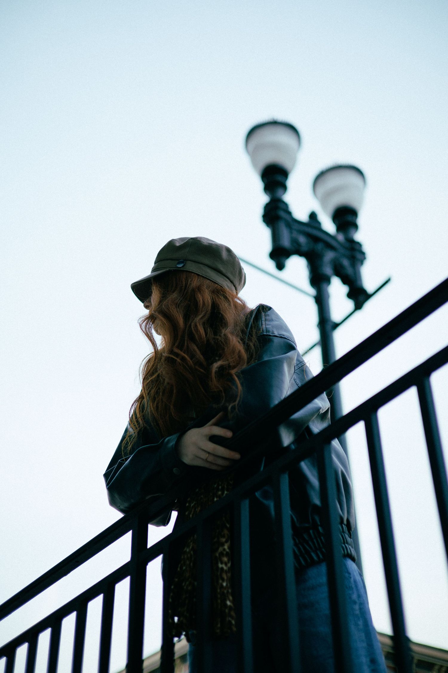 Artistic silhouette on metal railing during twilight wearing cap and jacket.