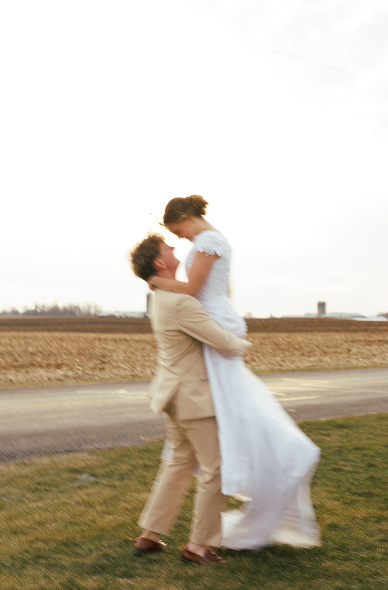 Couple in wedding attire dancing in a field at sunset creating a blurred motion effect.