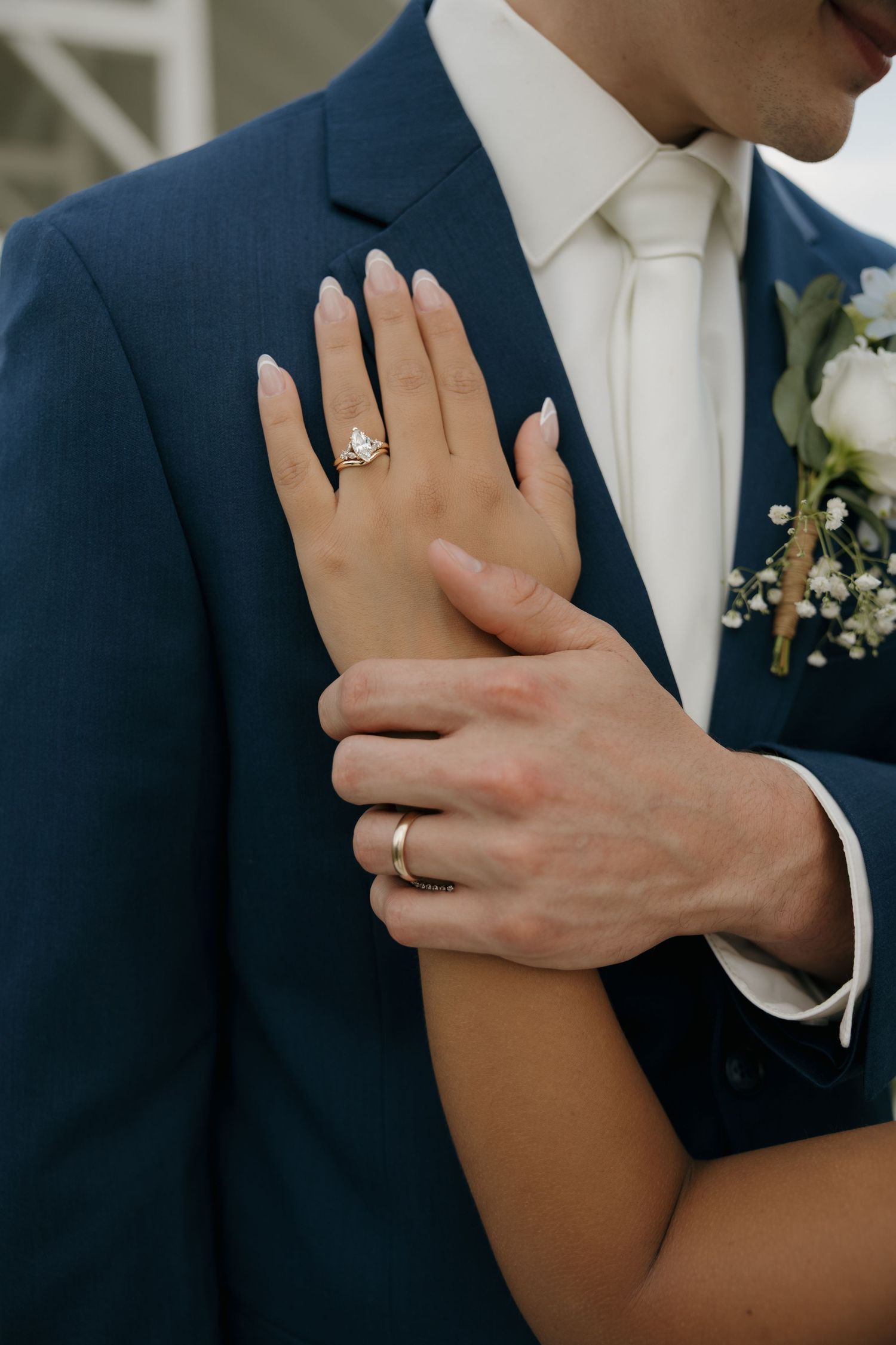 Close-up of bride and groom hands showing diamond engagement ring and gold wedding band on wedding day.