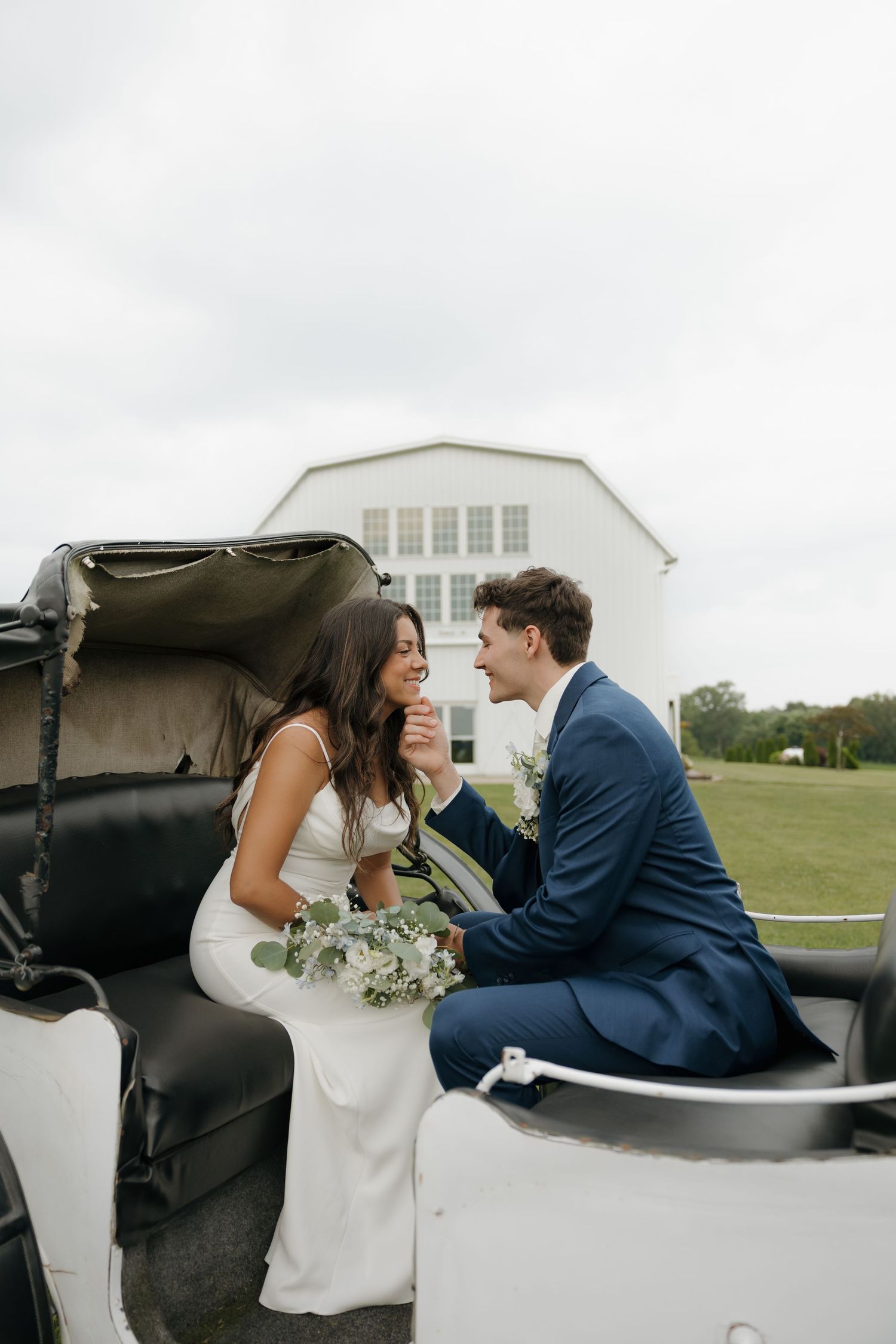 Bride and groom sitting together in a vintage car, sharing a romantic moment on their wedding day.