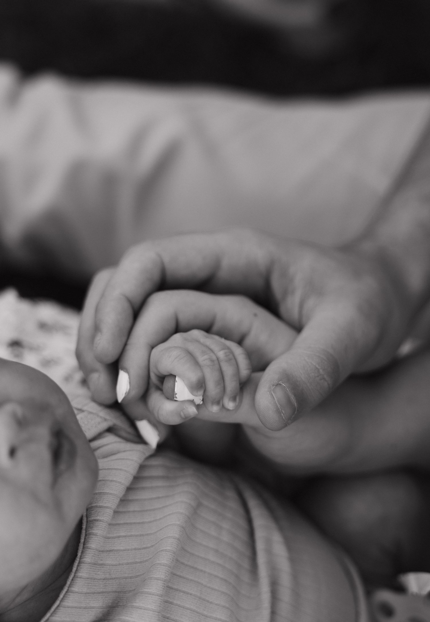 Close-up black and white photo of a newborn baby grasping a parents finger tenderly.