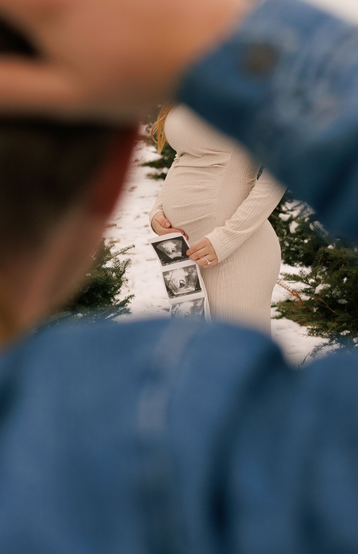 A close-up shot of hands holding a sonogram photo against snow and evergreen trees.