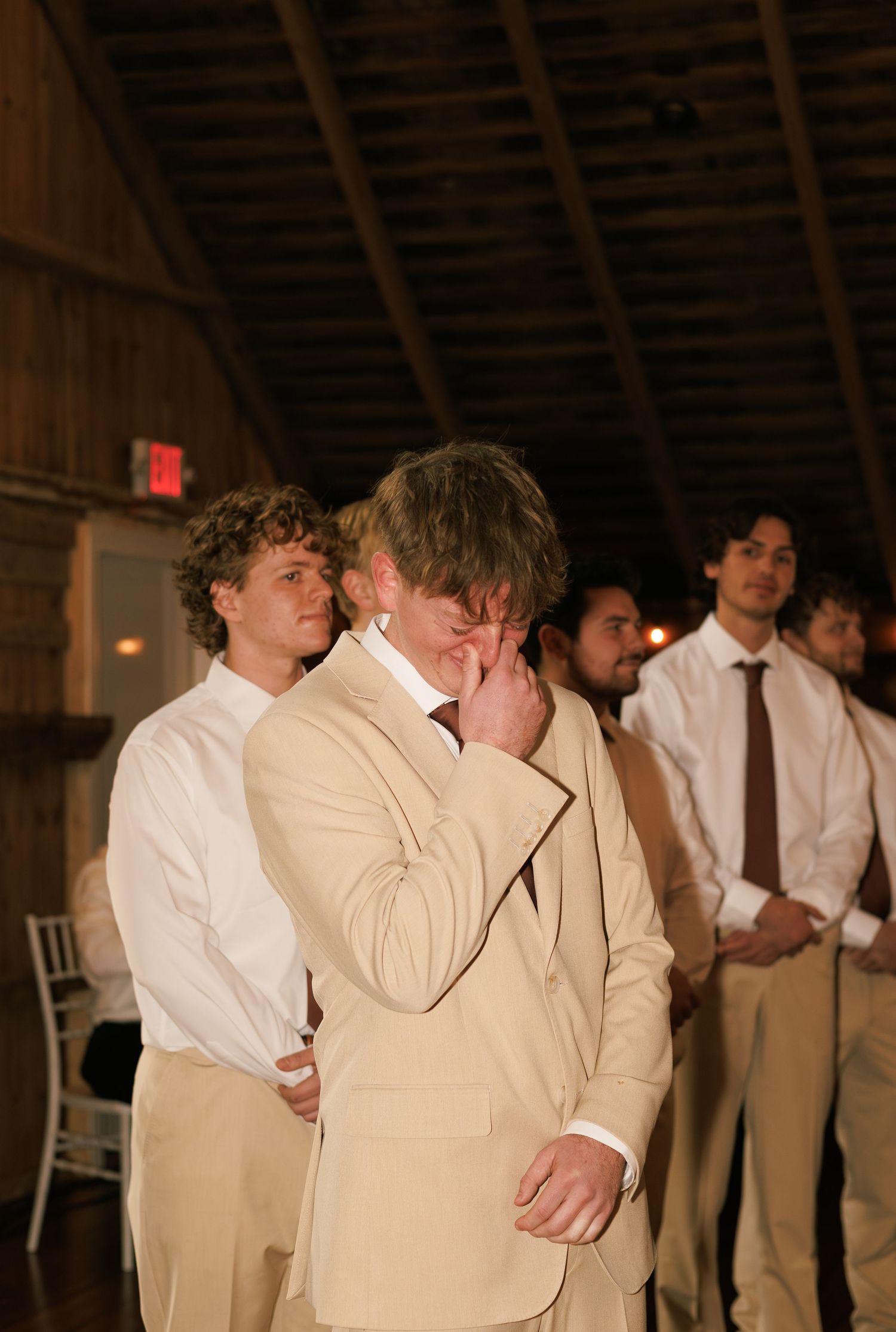 Groomsmen in tan suits and white shirts gathered at a rustic barn wedding.