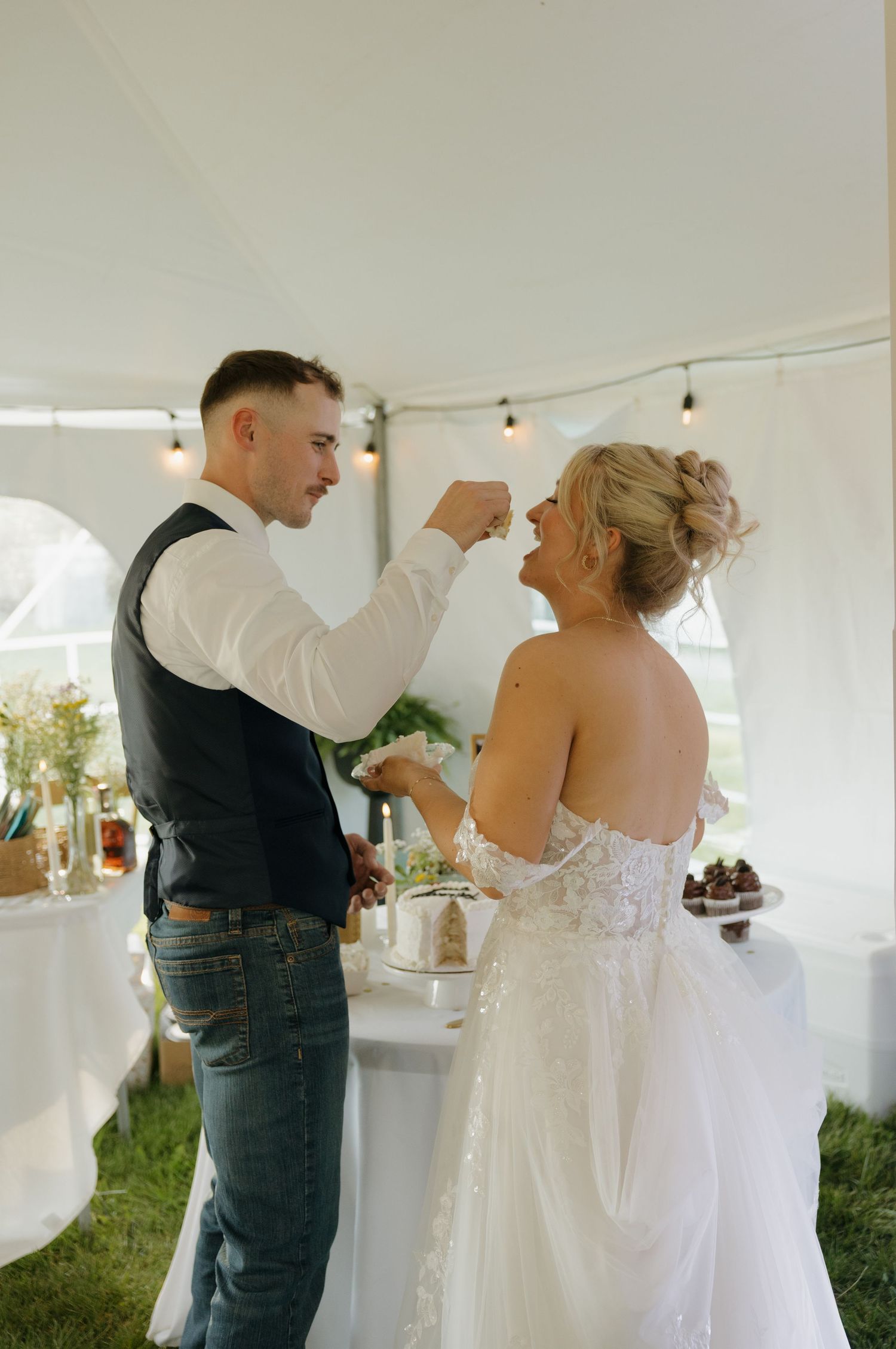 Groom feeding bride a bite of wedding cake during outdoor tent reception.