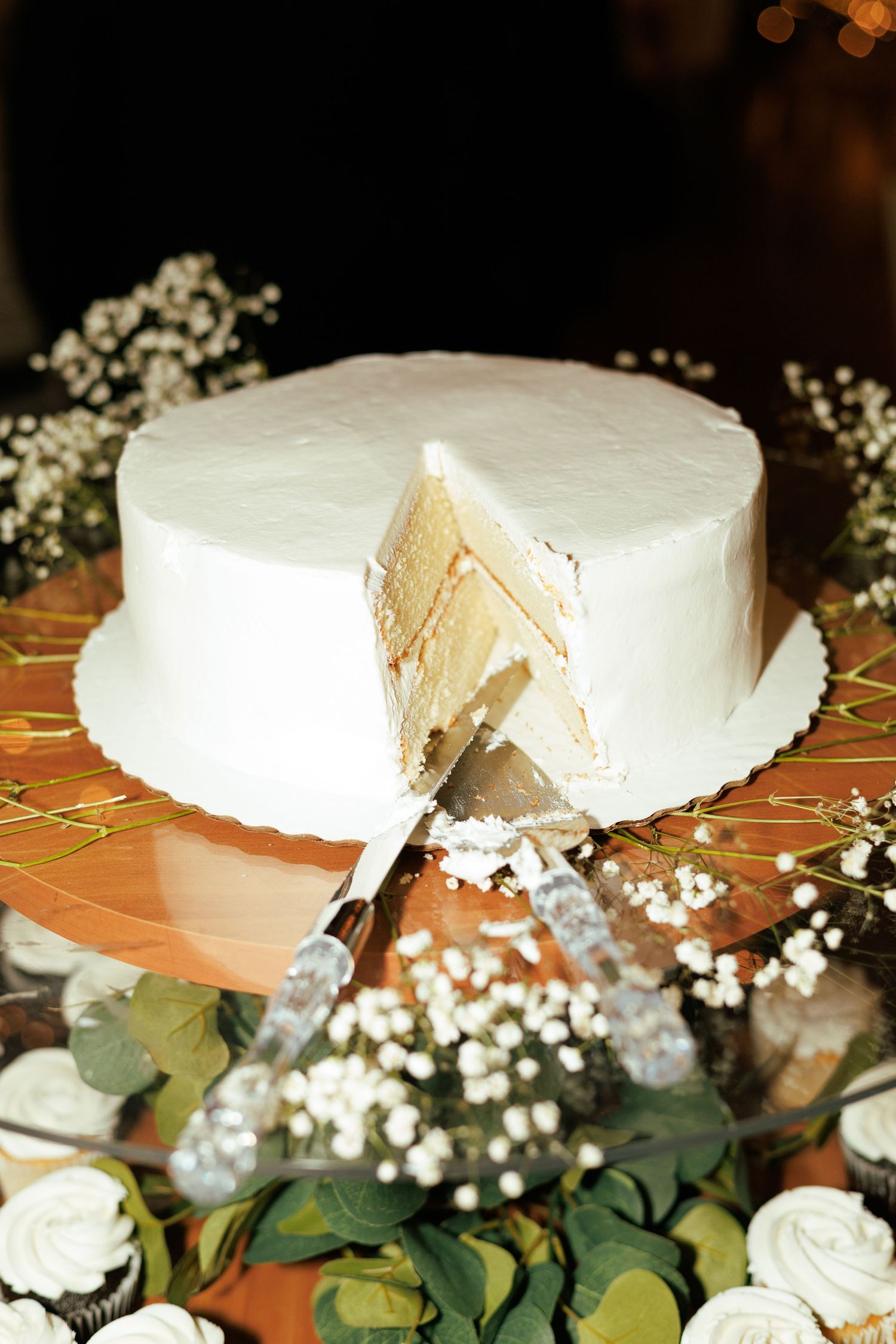 White wedding cake decorated with baby's breath and greenery on an orange tablecloth.
