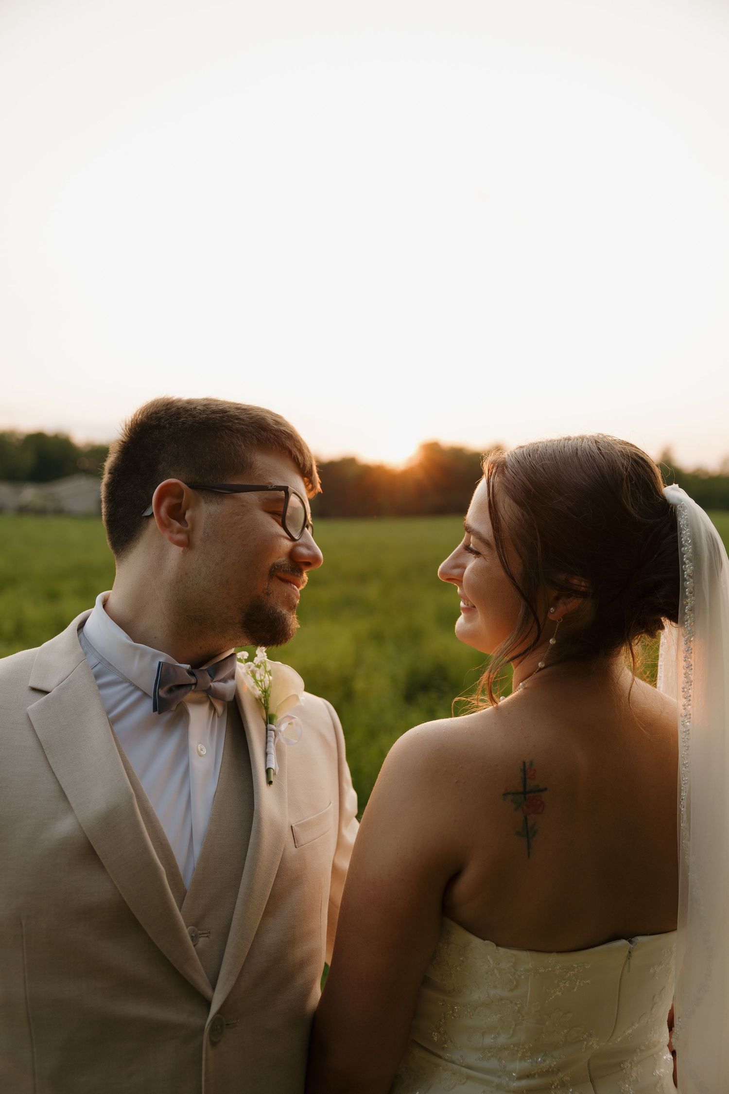 Bride and groom share a tender moment at golden hour, with cross tattoo visible on bride's back.
