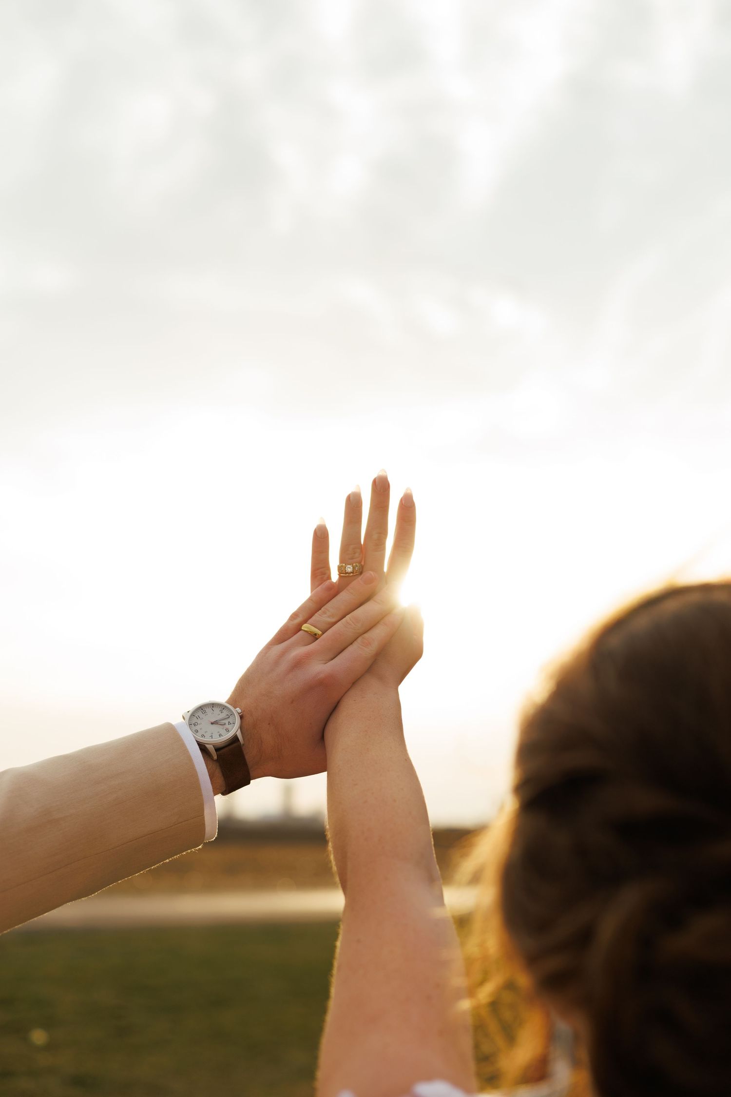 Silhouetted hands raised against a bright sunset sky.