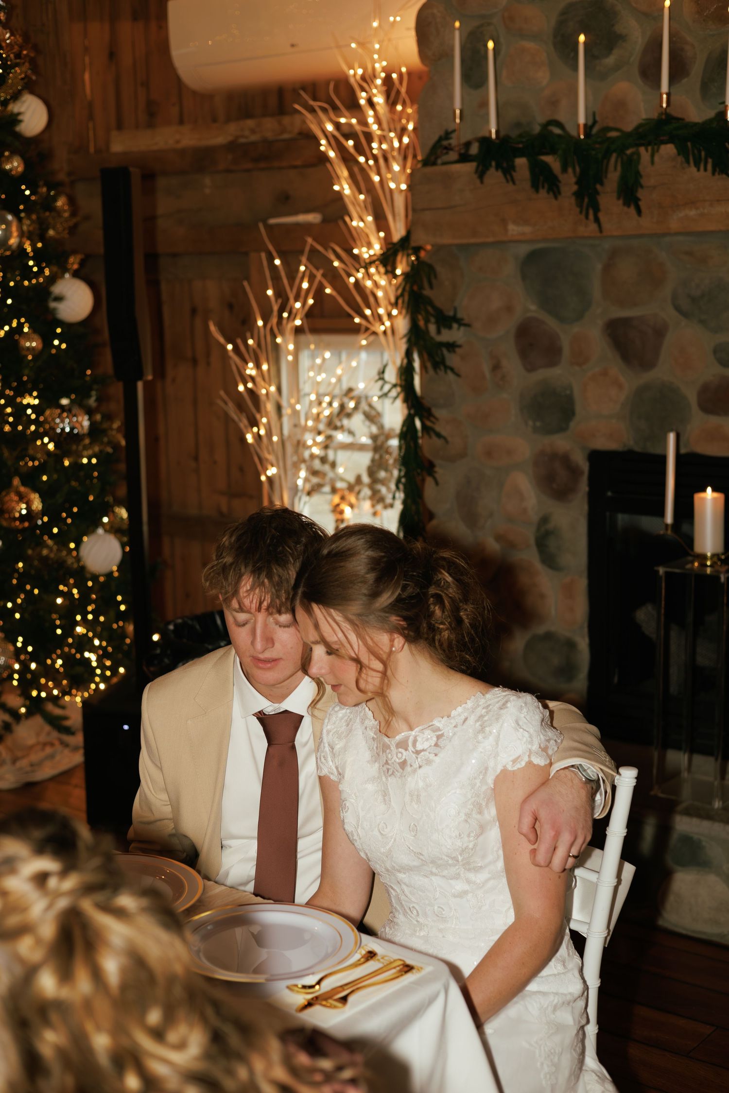 Newlyweds seated at reception table with sparklers and romantic lighting in rustic stone venue.
