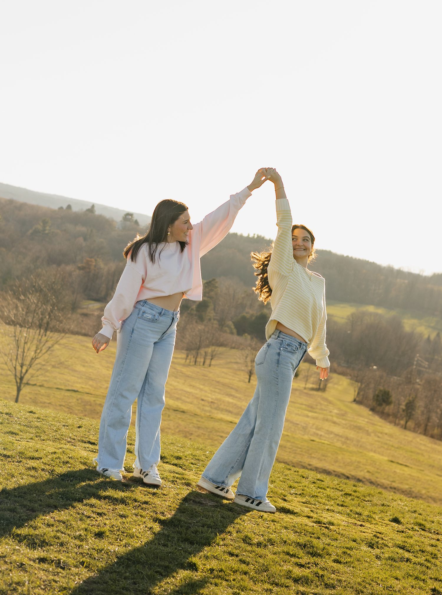 Candid photos of best friends dancing together in a sunlit meadow wearing matching light blue jeans.