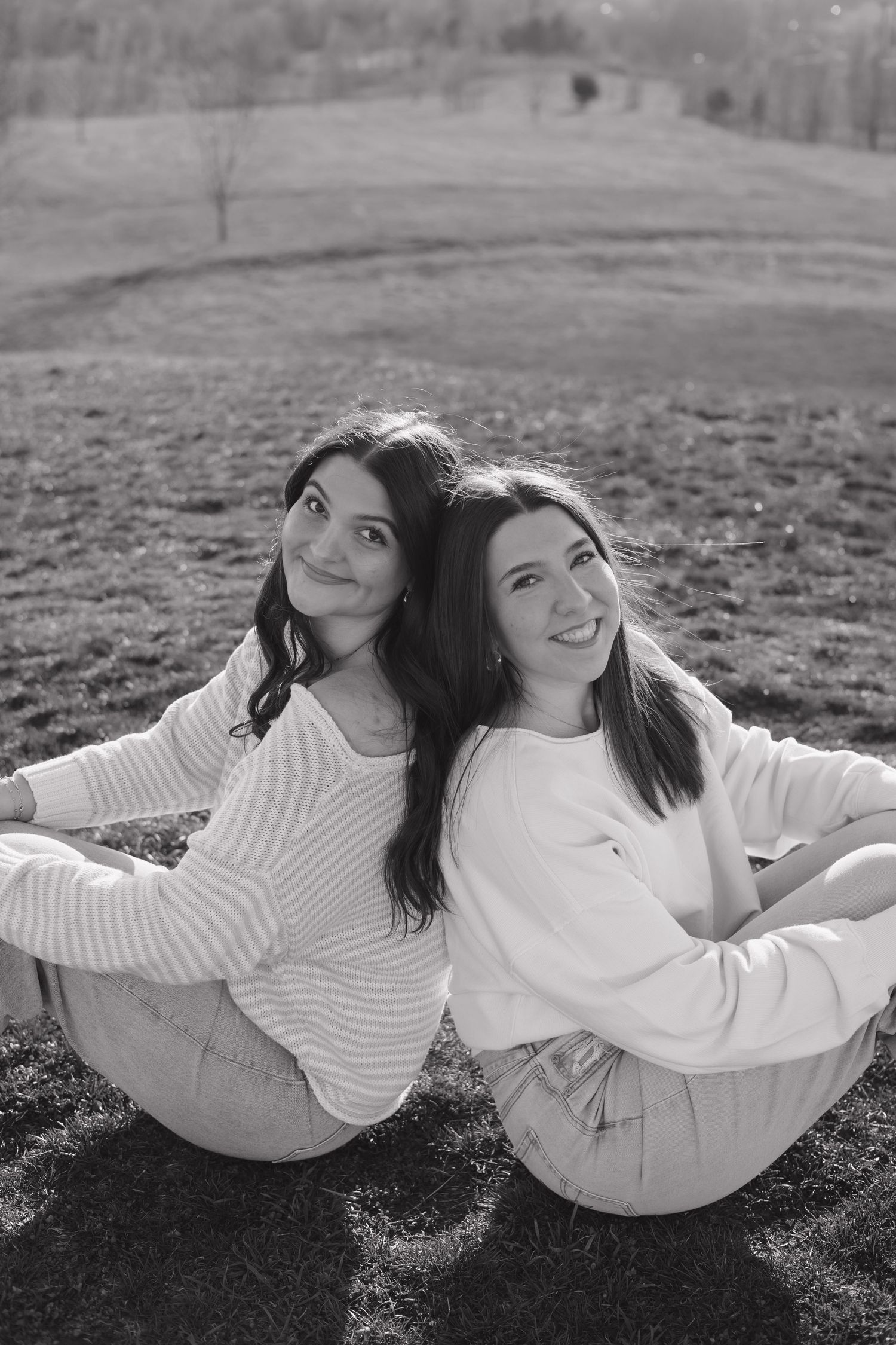 Two friends in matching white sweaters lying on grass in black and white photography.
