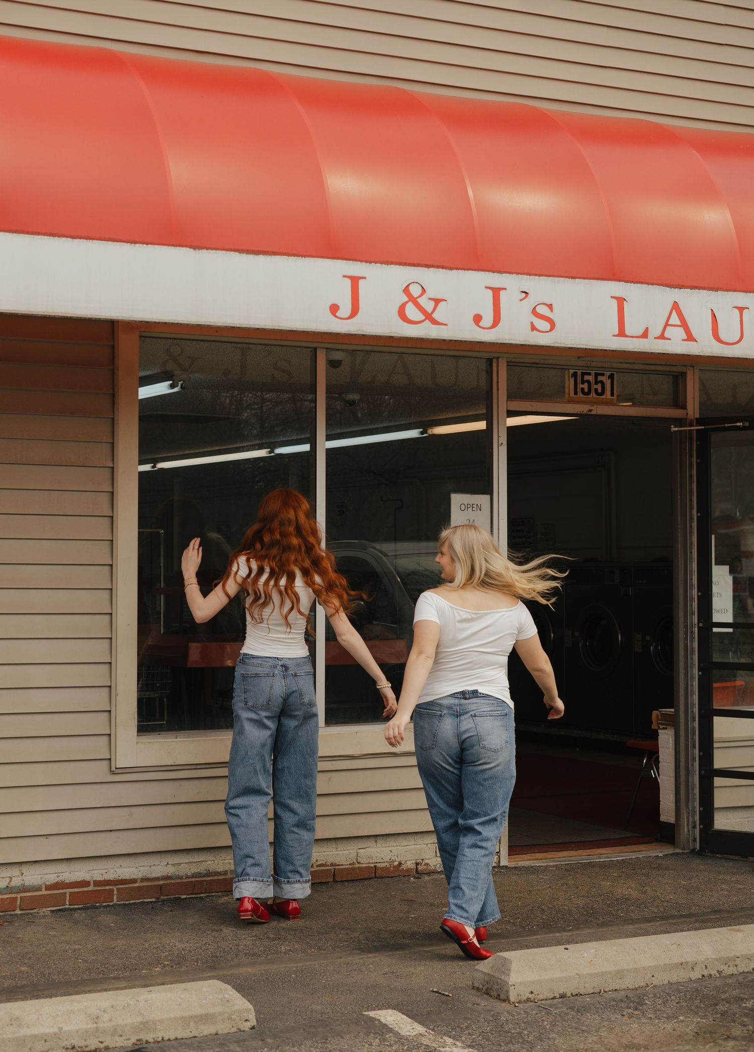 Two people in jeans walk toward a laundromat entrance in a strip mall setting.