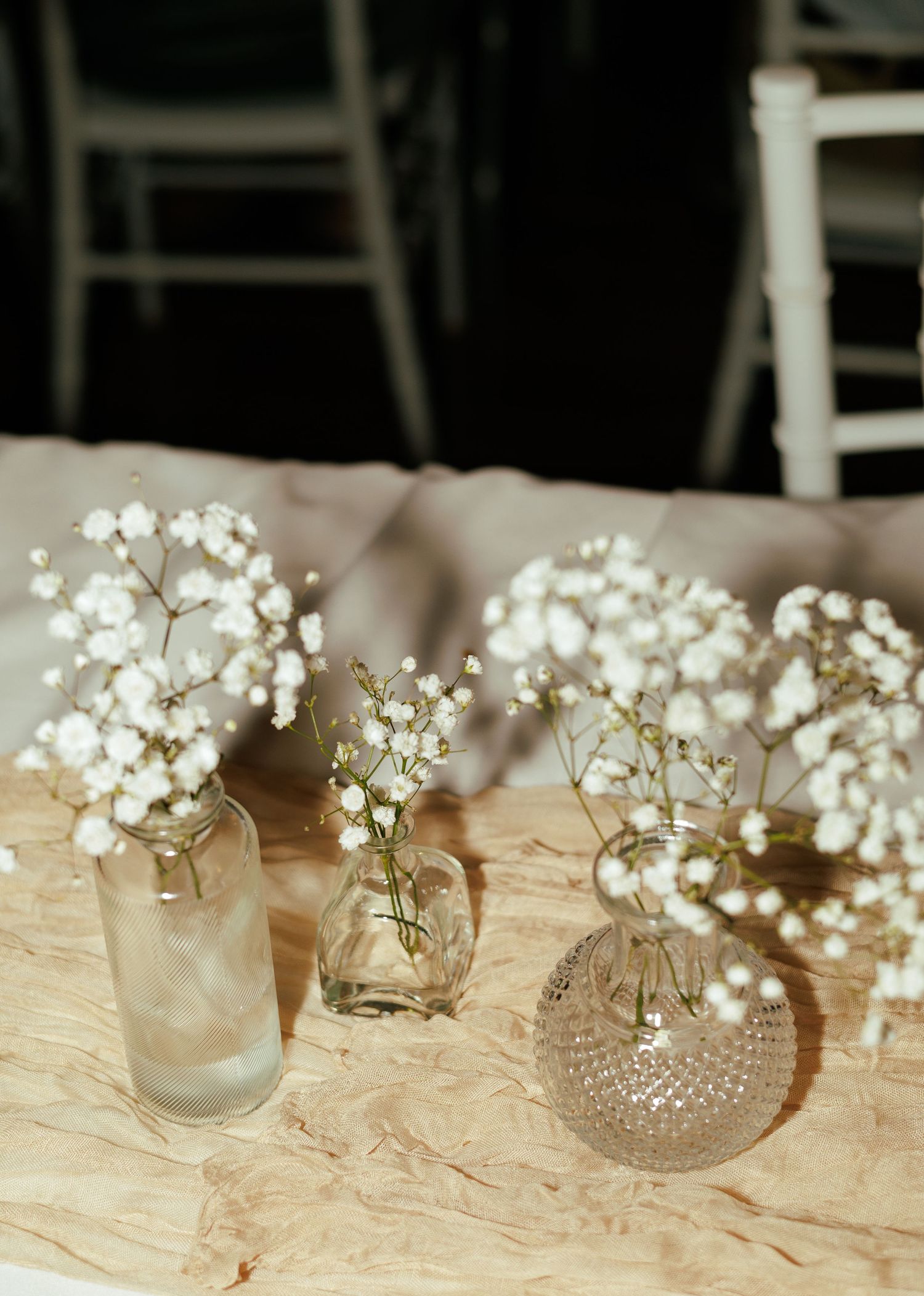 Small glass vases filled with baby's breath flowers arranged on a rustic table setting.