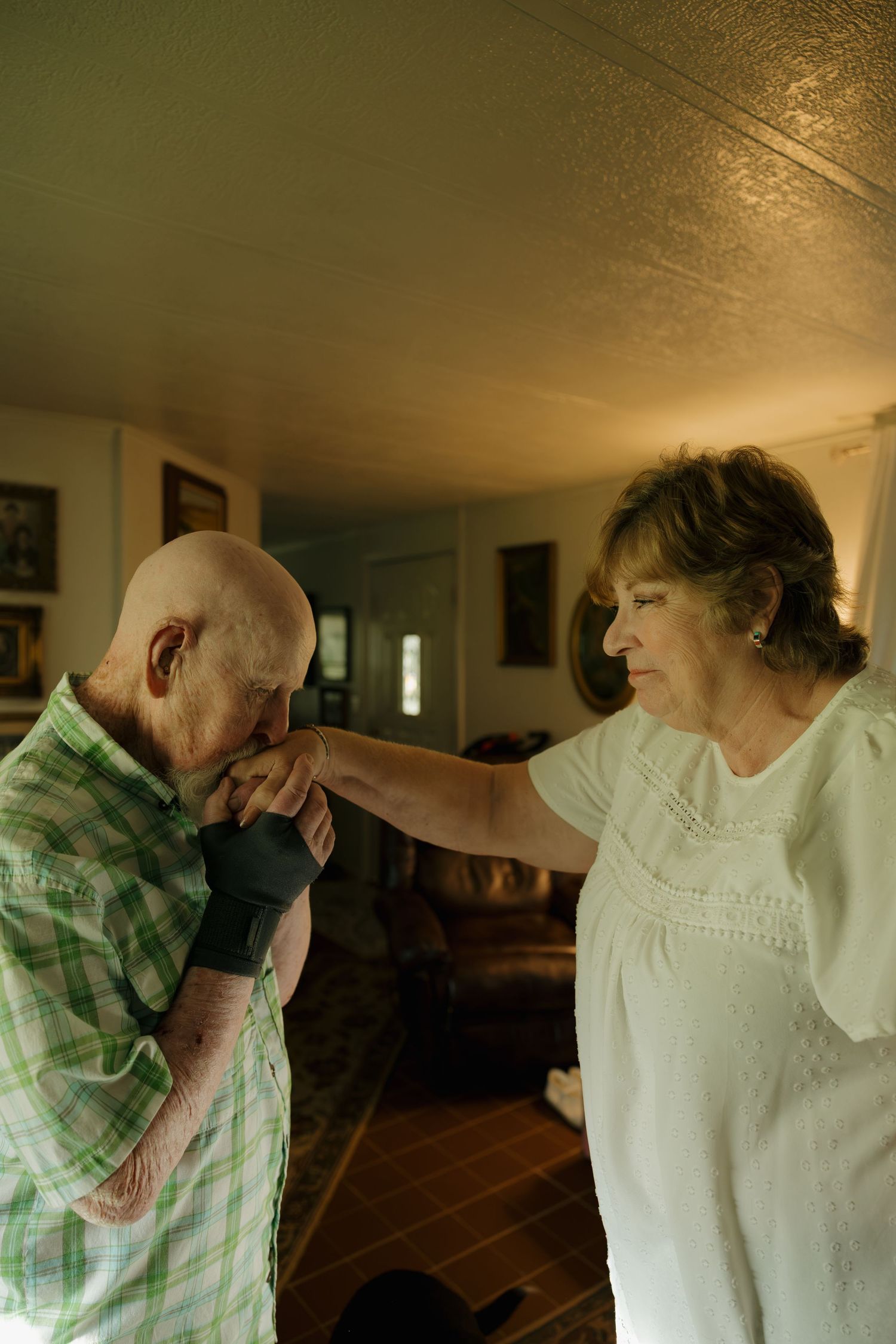 Elderly man kissing a woman's hand tenderly in a warmly lit living room, sharing a romantic and heartfelt moment.