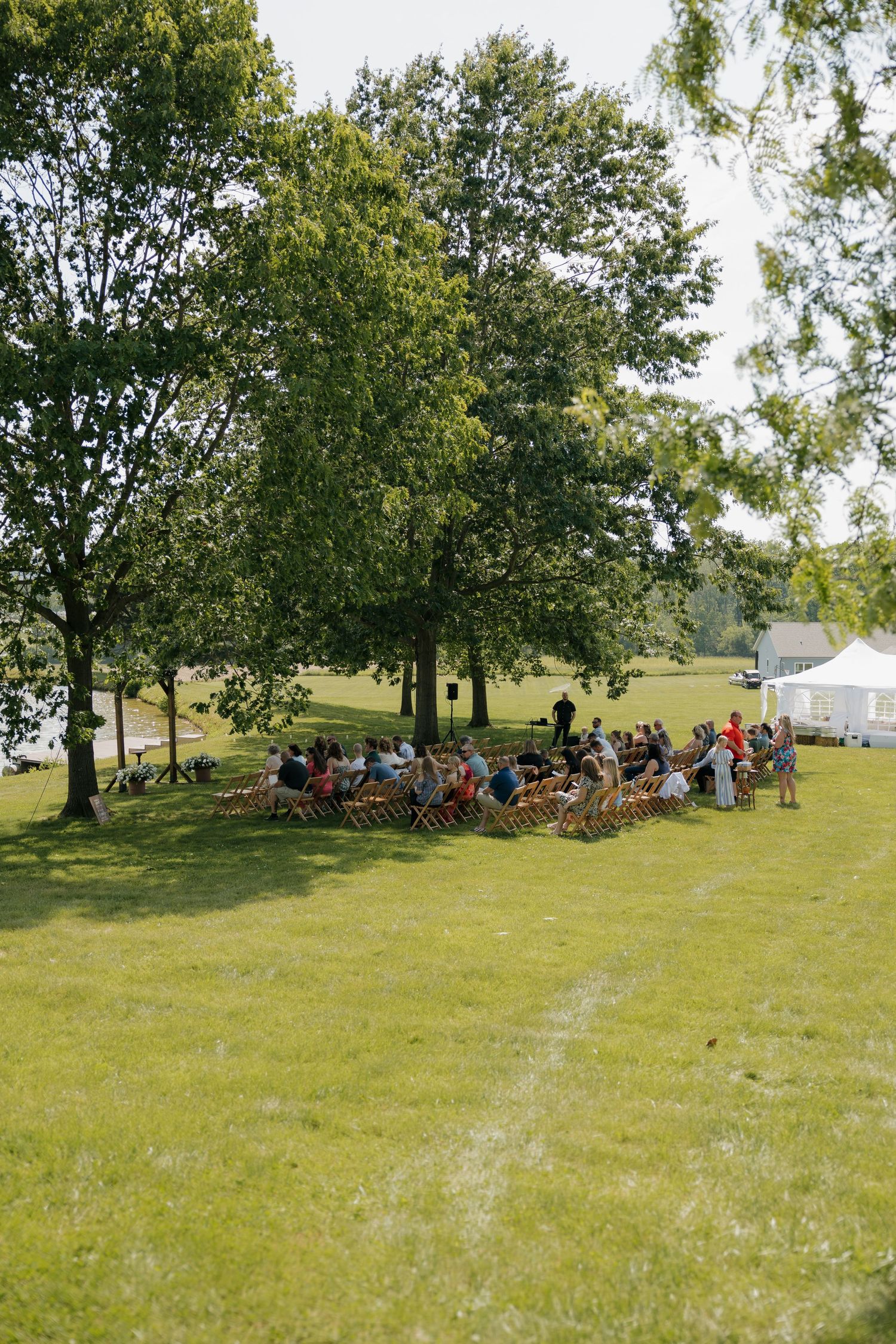 Guests seated in wooden chairs outdoors under trees for a garden wedding ceremony.